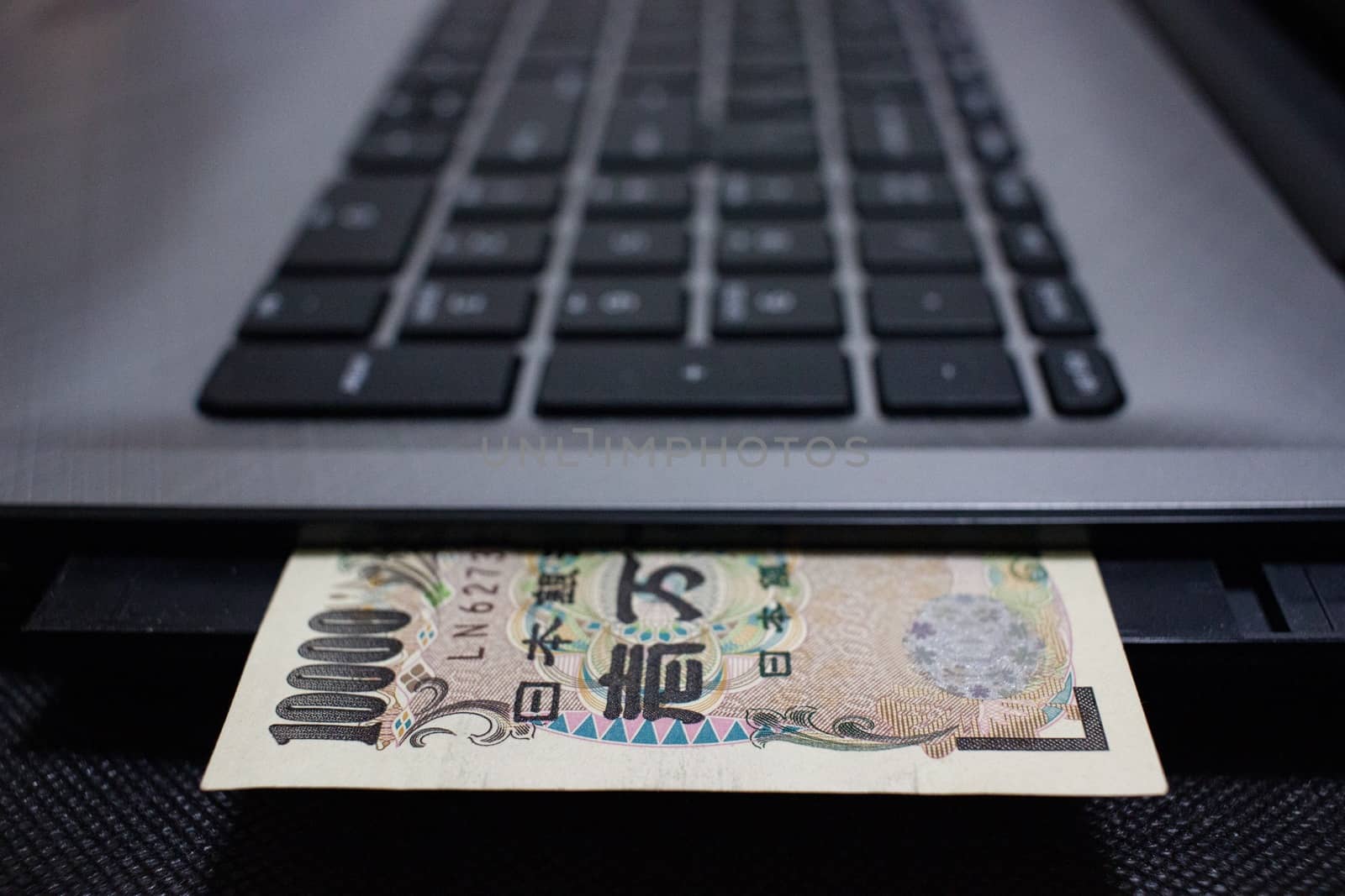 Japanese bank note protruding from a laptop computer.