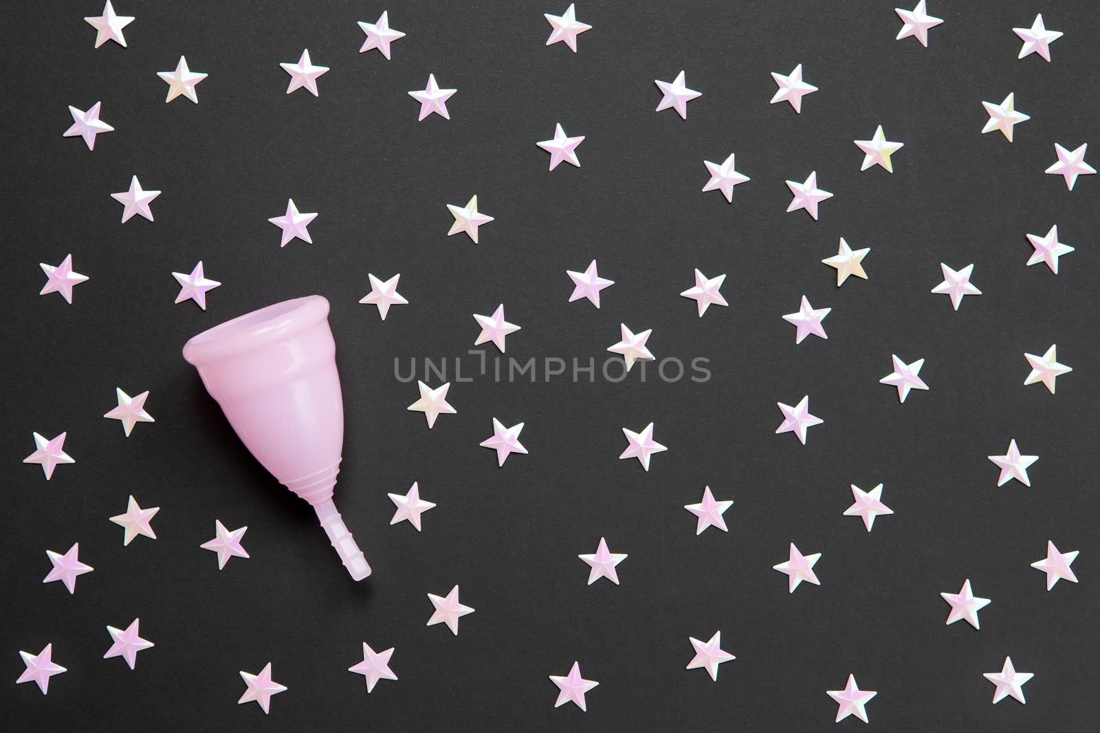 Pink menstrual cup on black background with numerous stars. Concept possibility of use cup at night, zero waste, savings, minimalism. Feminine hygiene product, flat lay, copy space. Horizontal.