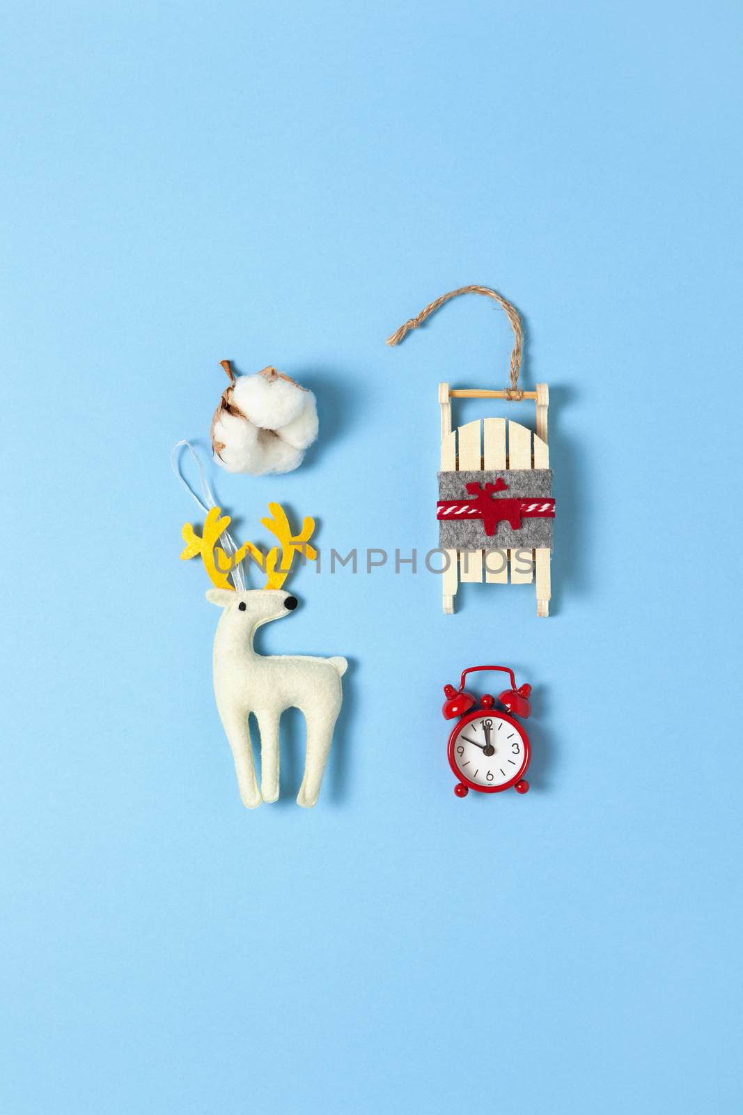 Simple creative Christmas composition. Cotton box, deer, wooden sled, alarm clock on blue background, copy space. Minimal style. Top view. Vertical. For social media, greeting card, office supplies.