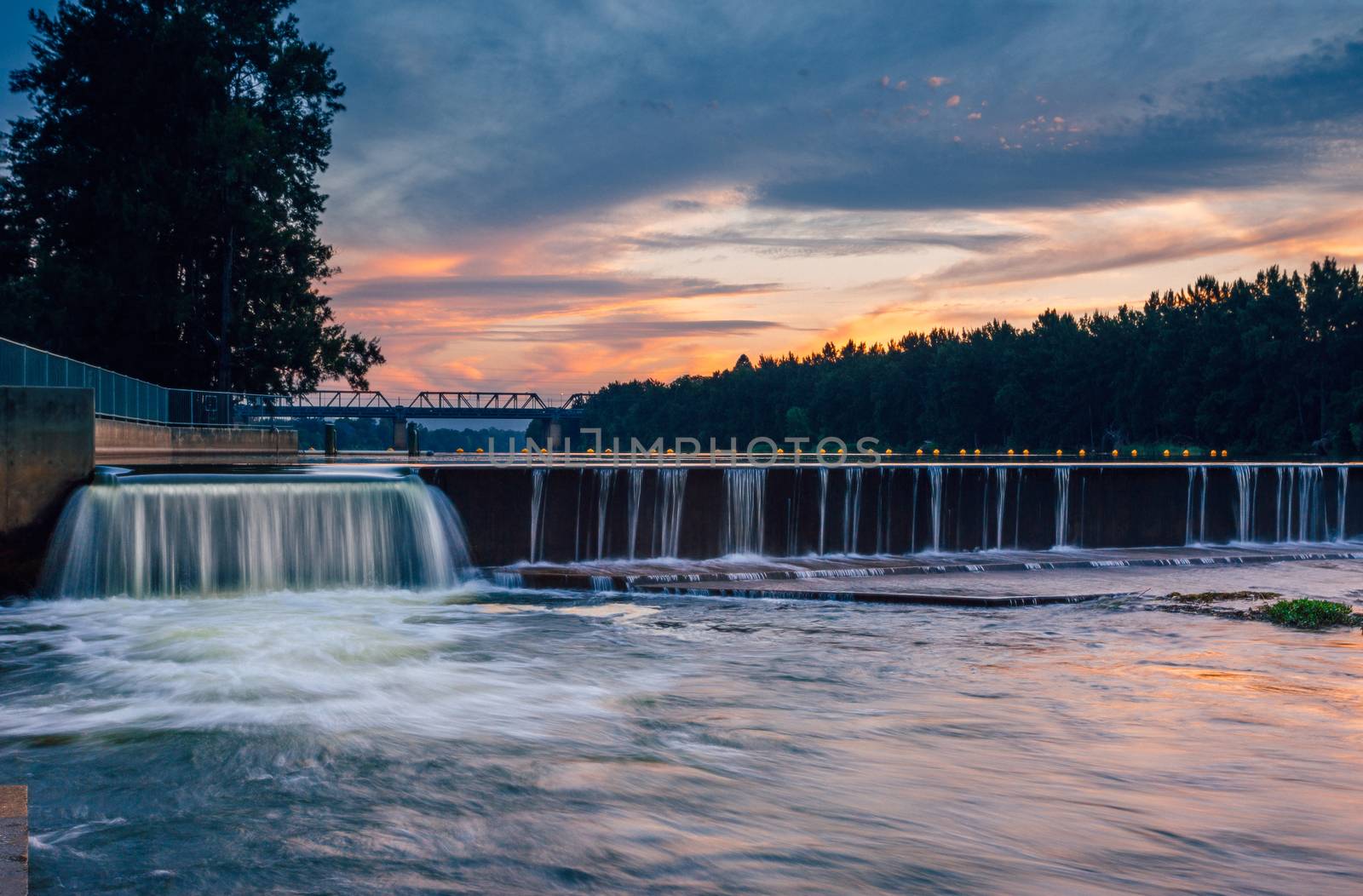 The overflow at Penrith Weir as the sunset colours some of the clouds in the sky and reflects in the rushing waters below.