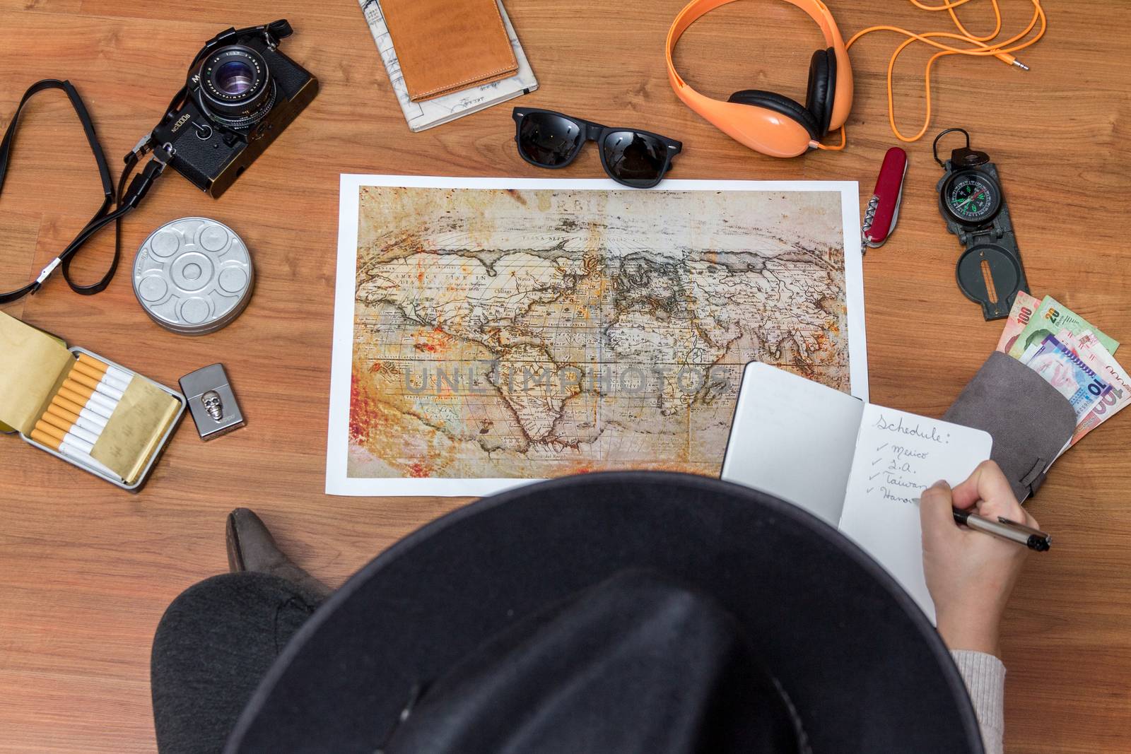 Young woman planning vacation using world map and compass along with other travel accessories. Tourist wearing brown hat looking at the world map.