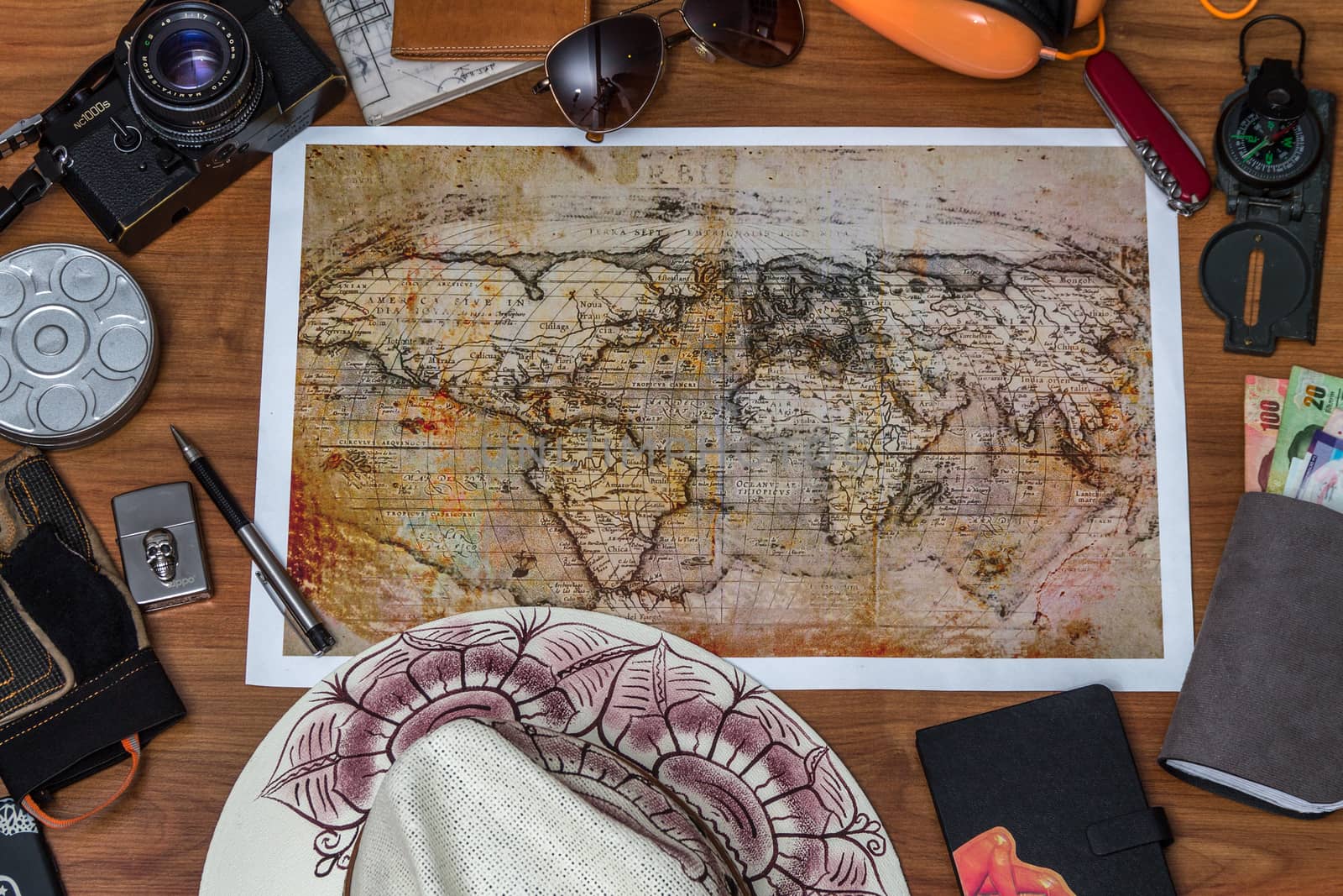 Man planning vacation using world map and compass along with other travel accessories. Tourist wearing brown hat looking at the world map