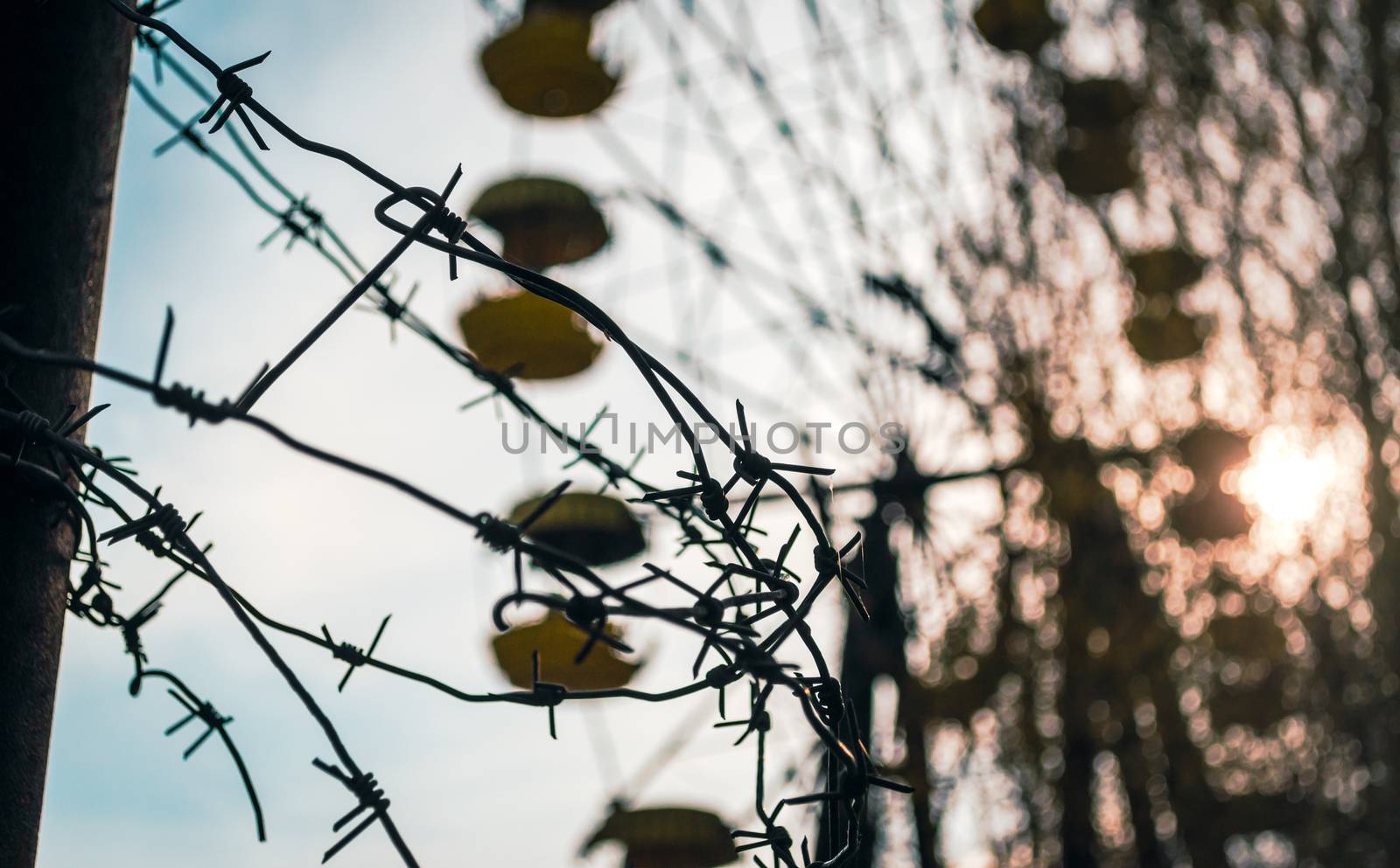 barbed wire on the background of a carousel and the setting sun among the trees in the amusement park in Chernobyl Ukraine in autumn