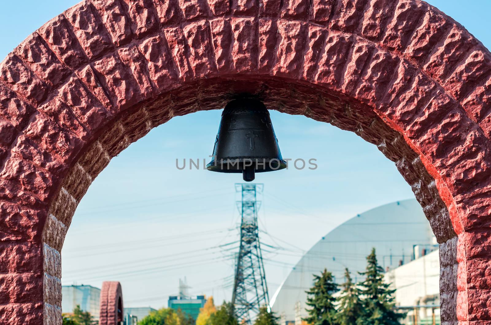 christian church bell in a stone arch on the background of a nuclear power plant and blue sky in Chernobyl Ukraine autumn day