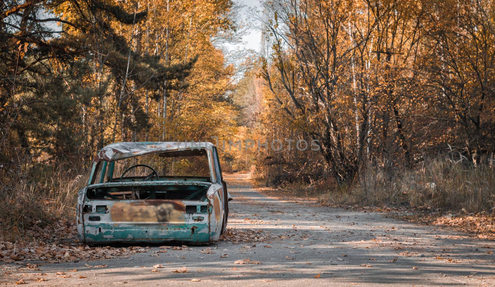 road with a broken car with trees and fallen leaves in Chernobyl Ukraine in autumn
