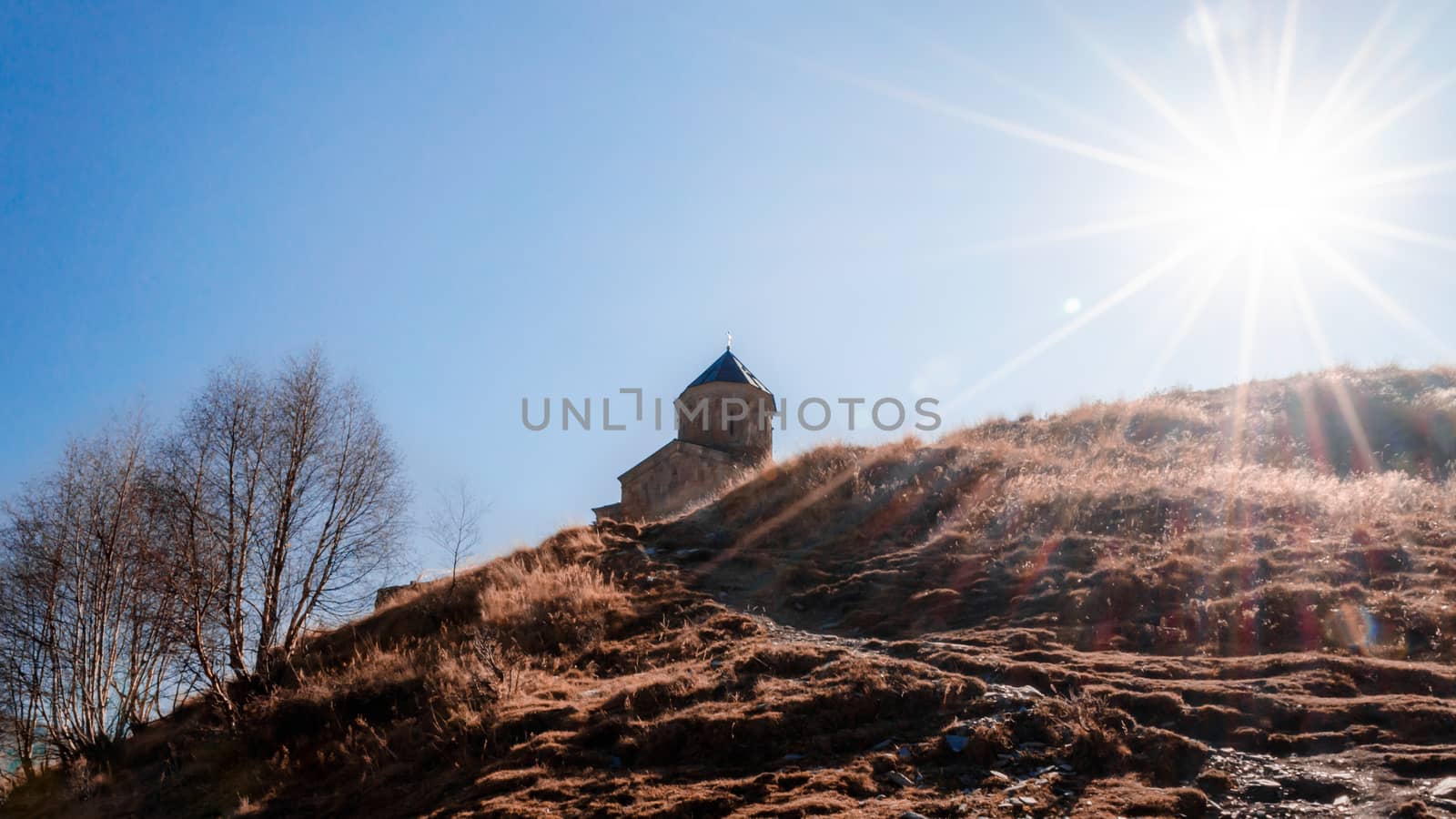 landscape church on the mountain against the background of the sun and sun rays and blue sky in Georgia in the autumn afternoon