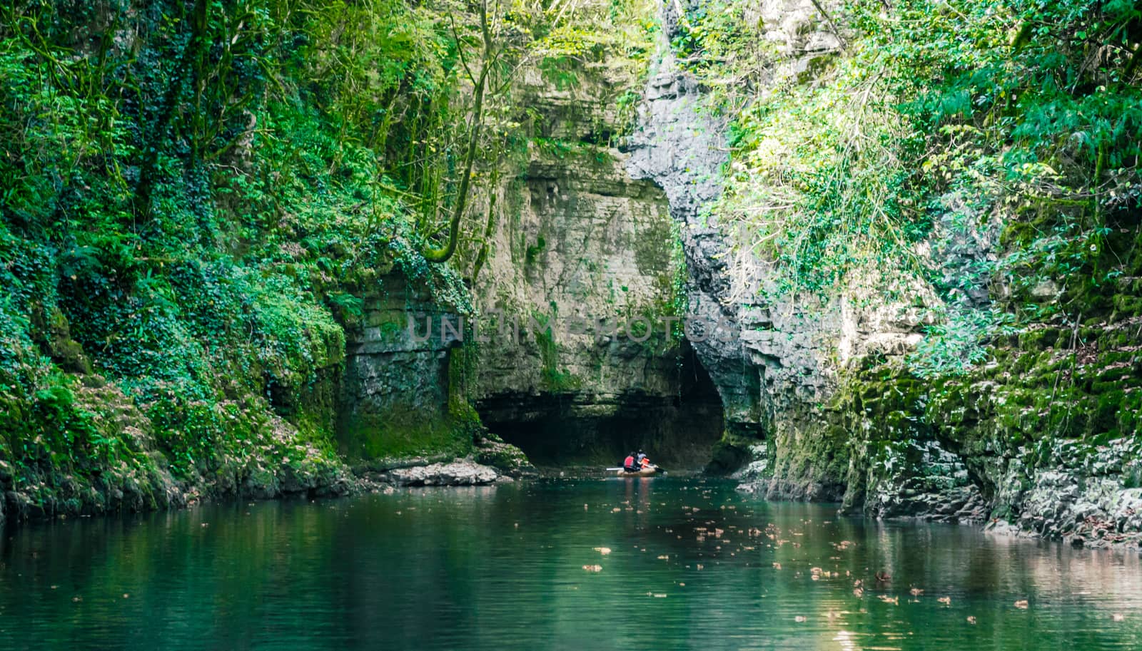 mountain river with tall cliffs and green plants and tourists in a boat in a canyon in Georgia in autumn