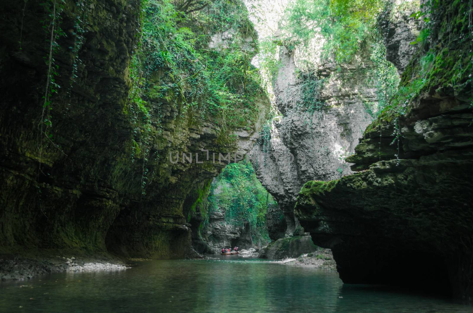 mountain river with tall cliffs and green plants and tourists in a boat in a canyon in Georgia in autumn