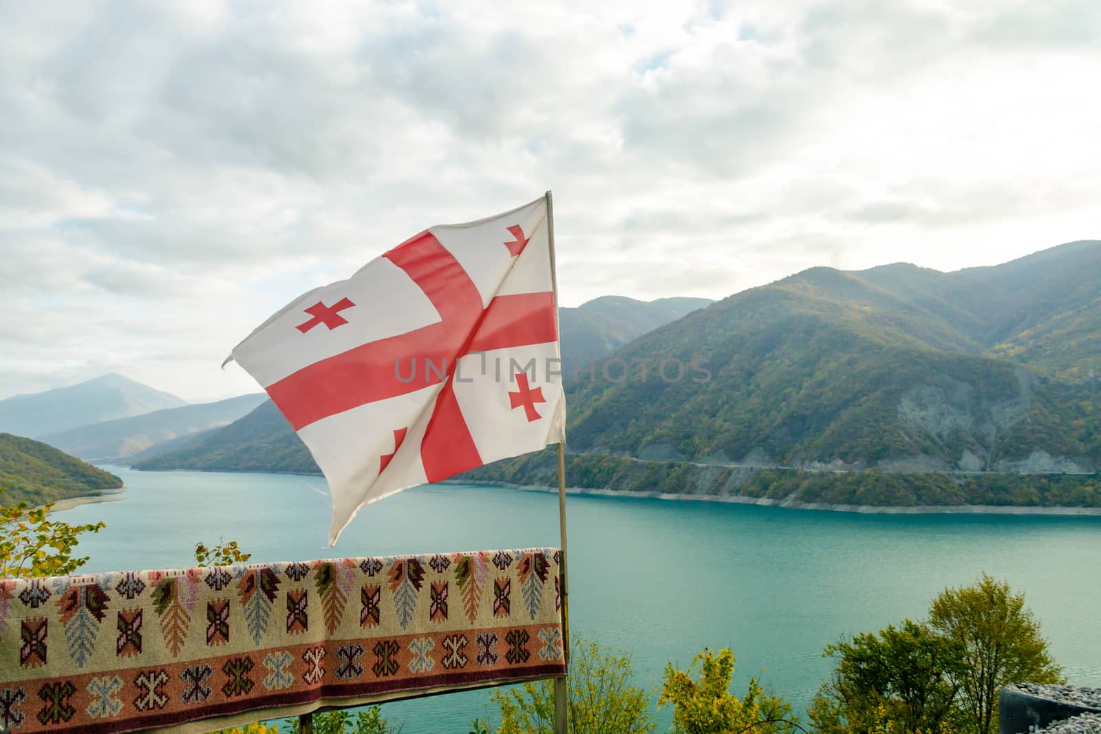 Georgia country flag on the background of a mountain landscape with forest and lake and sky with clouds