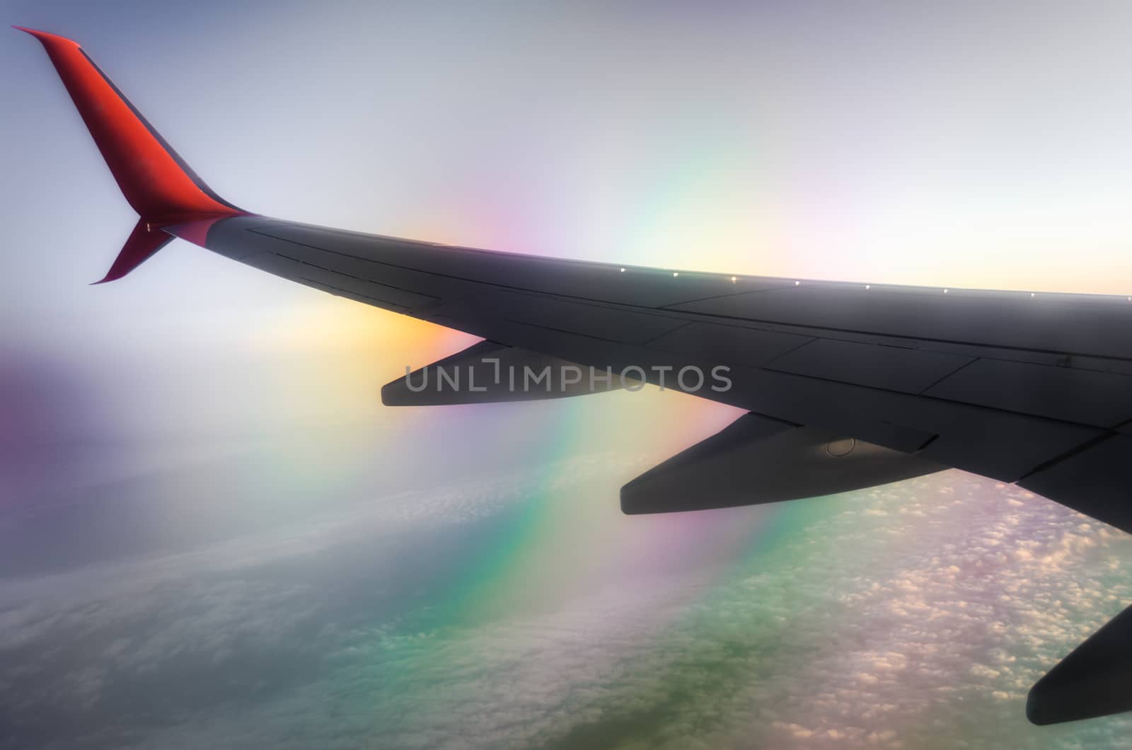 wing of a civilian airliner in flight above clouds with color optical effect