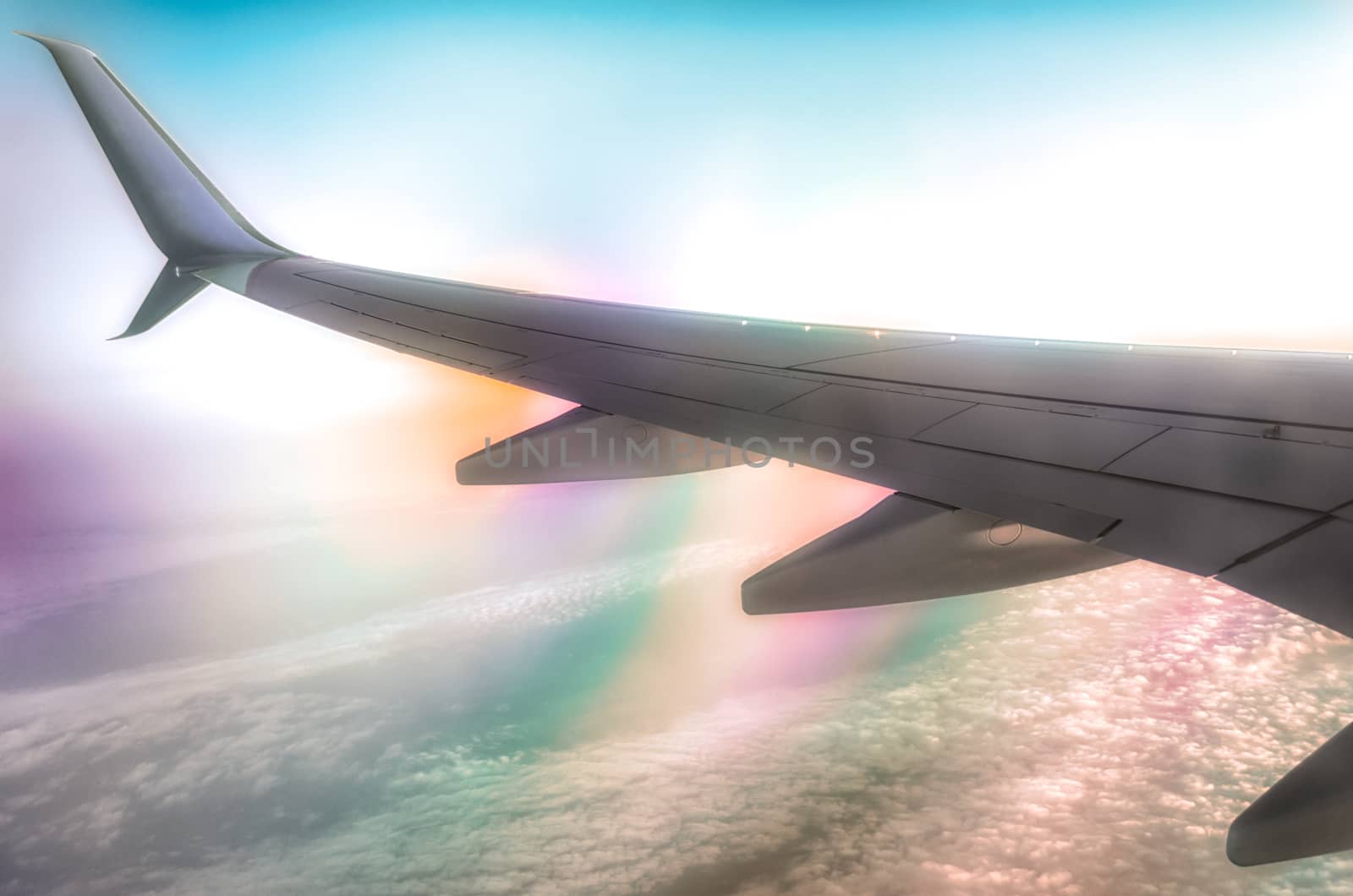 wing of a civilian airliner in flight above clouds with color optical effect
