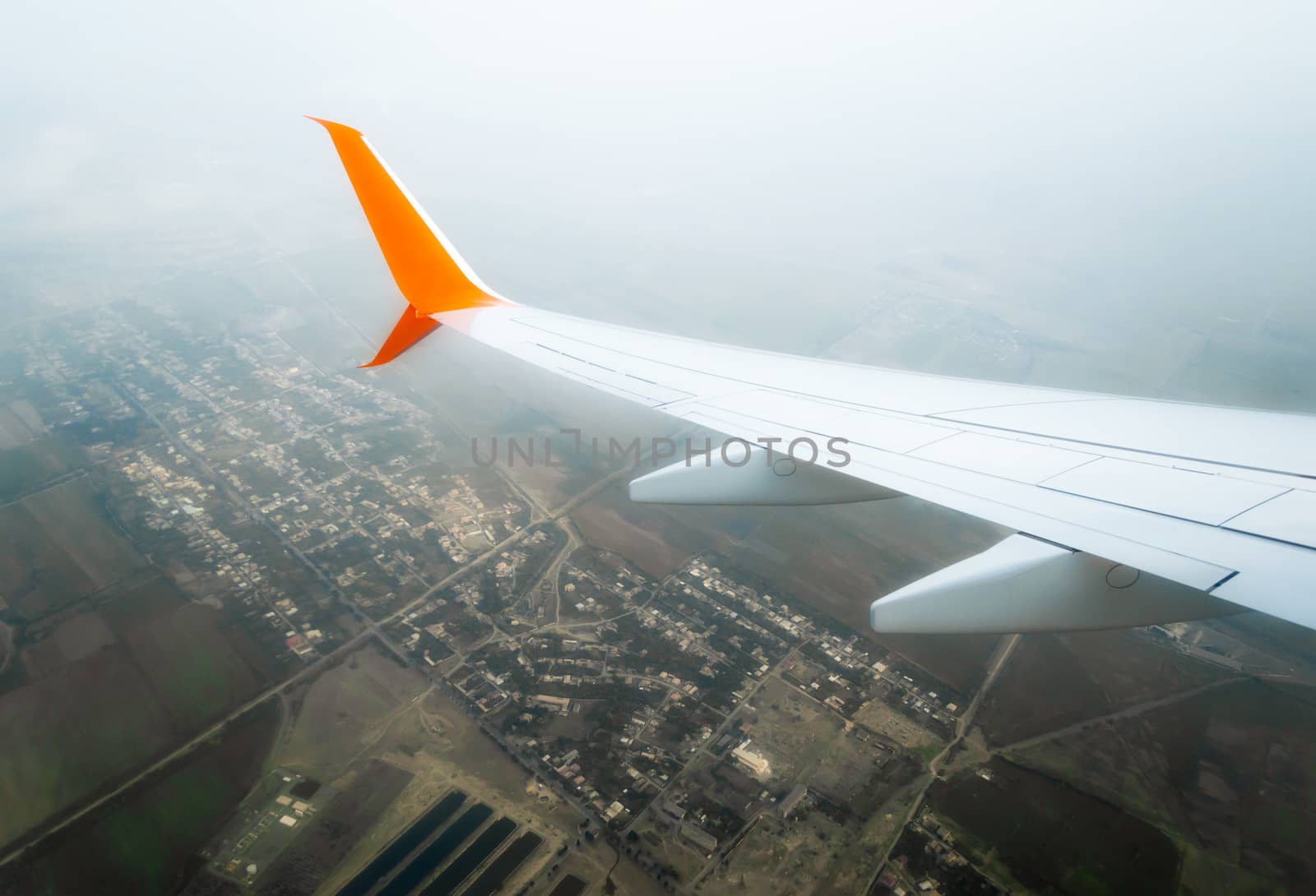 wing of a flying civil airliner over a city and fields Georgia Tbilisi