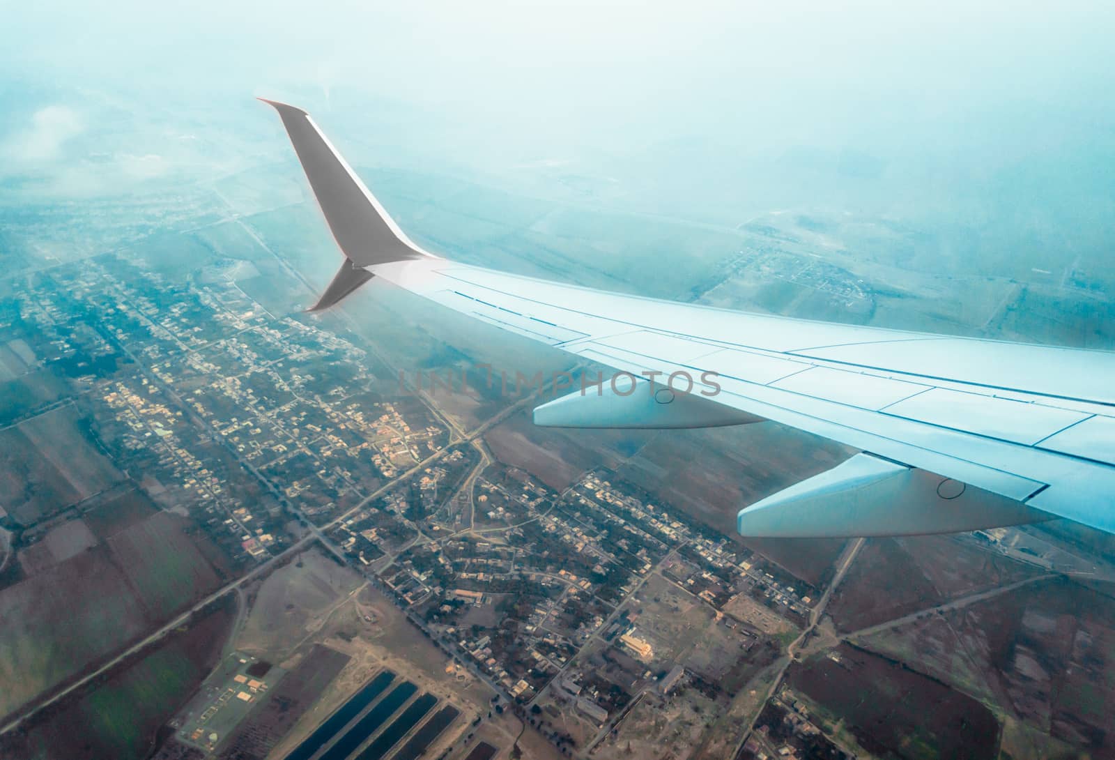 wing of a flying civil airliner over a city and fields Georgia Tbilisi