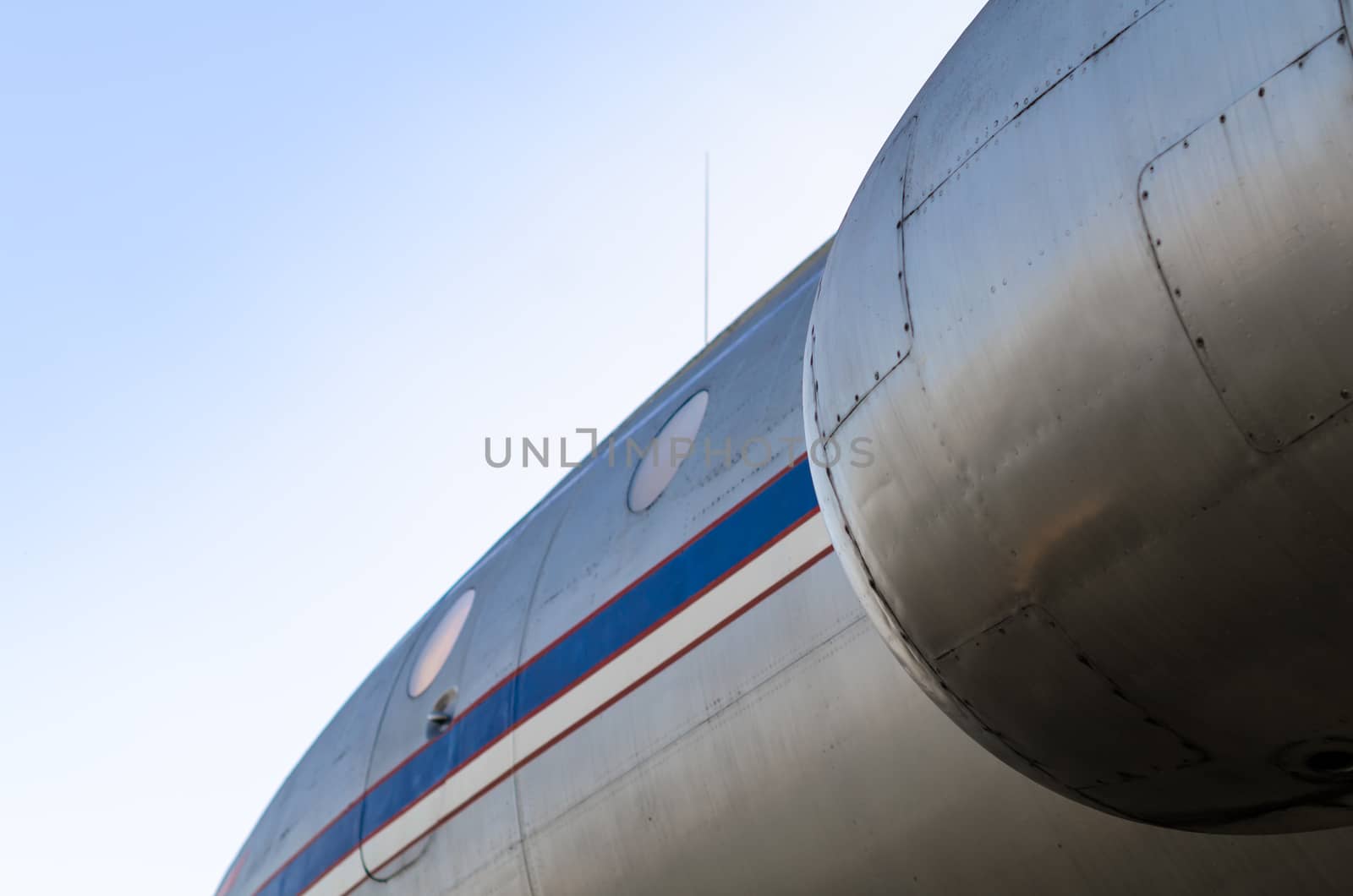 background airplane body with blue and white stripe with portholes and turbine close up