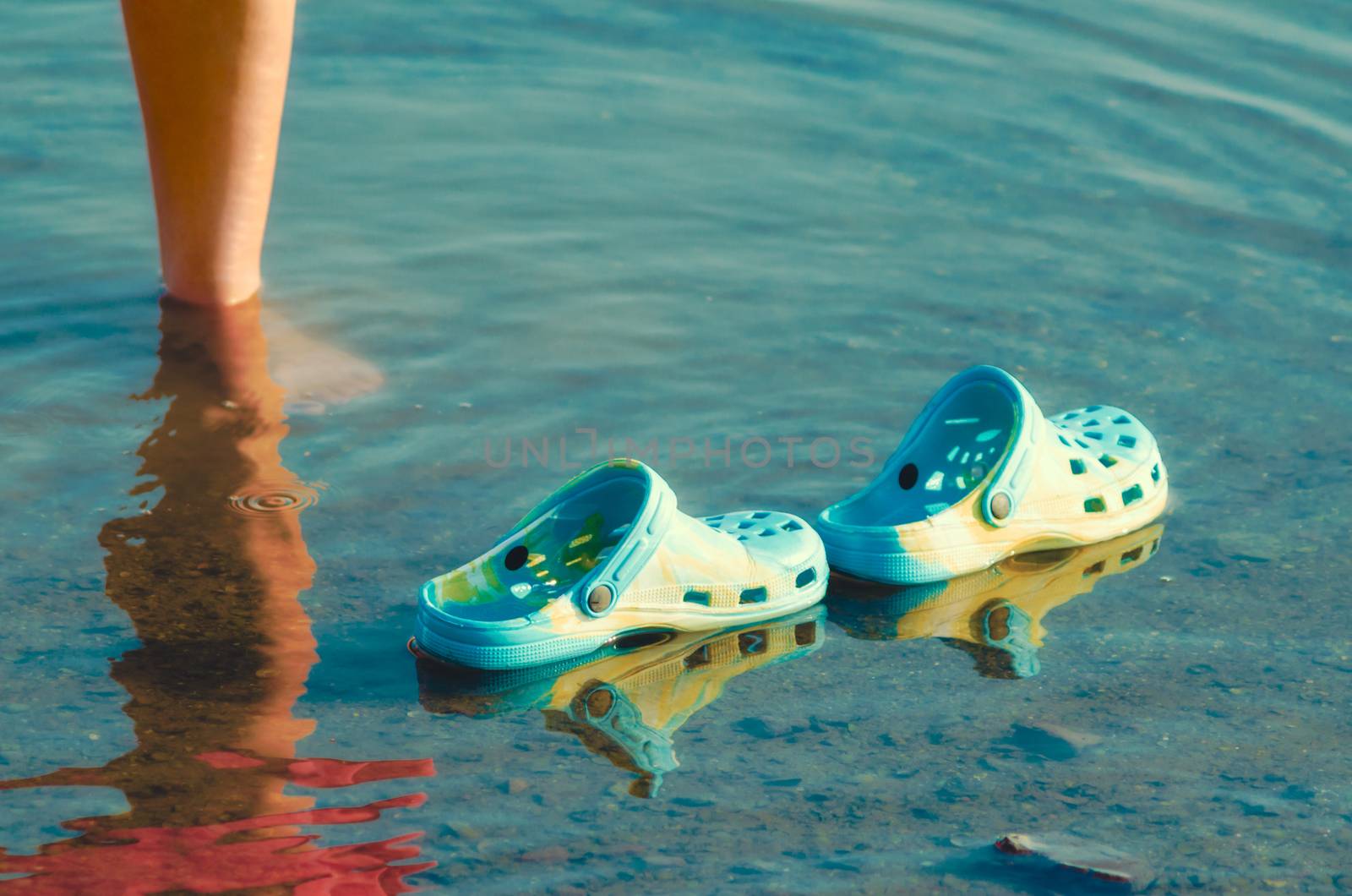 rubber slippers float in clear water next to female legs closeup