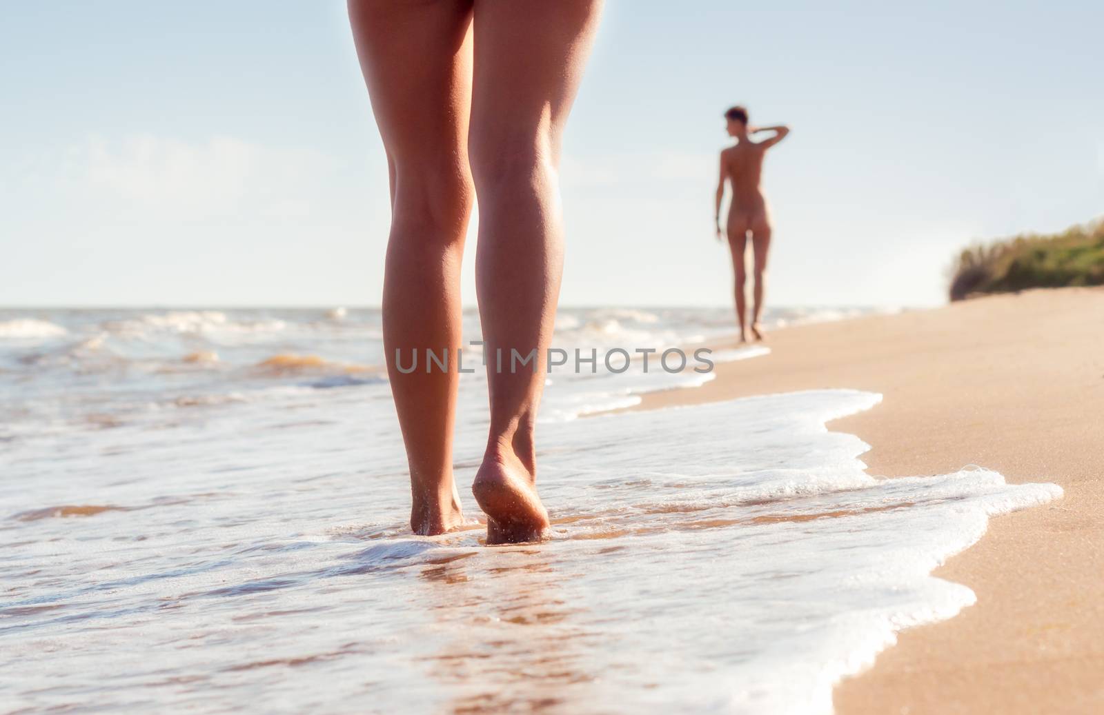nude young girls walk on the beach in the waves of the surf on a summer day