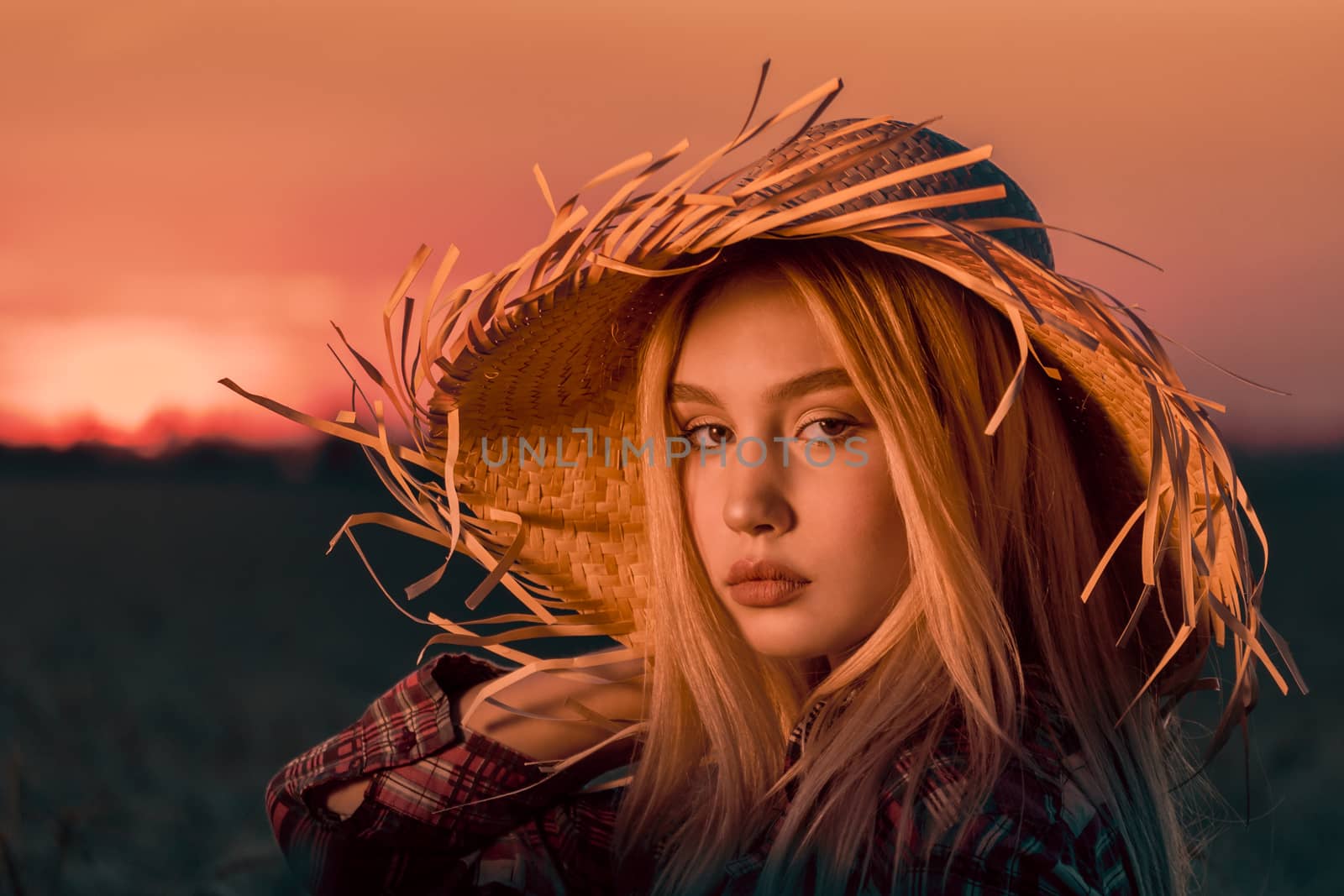 portrait of a young girl with blond hair in a straw hat in the evening at sunset in summer close up