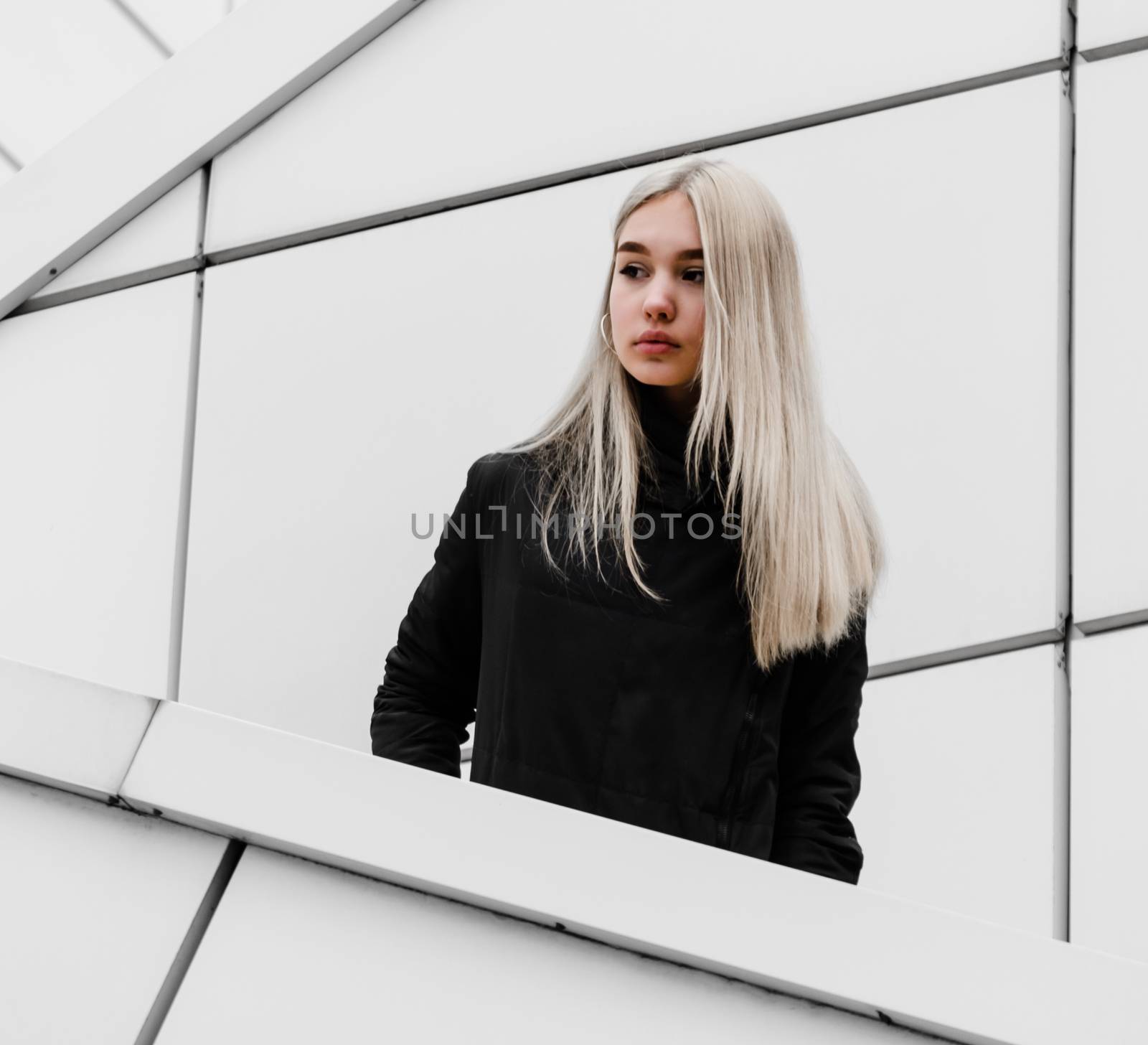 young blonde girl in black clothes against a gray building