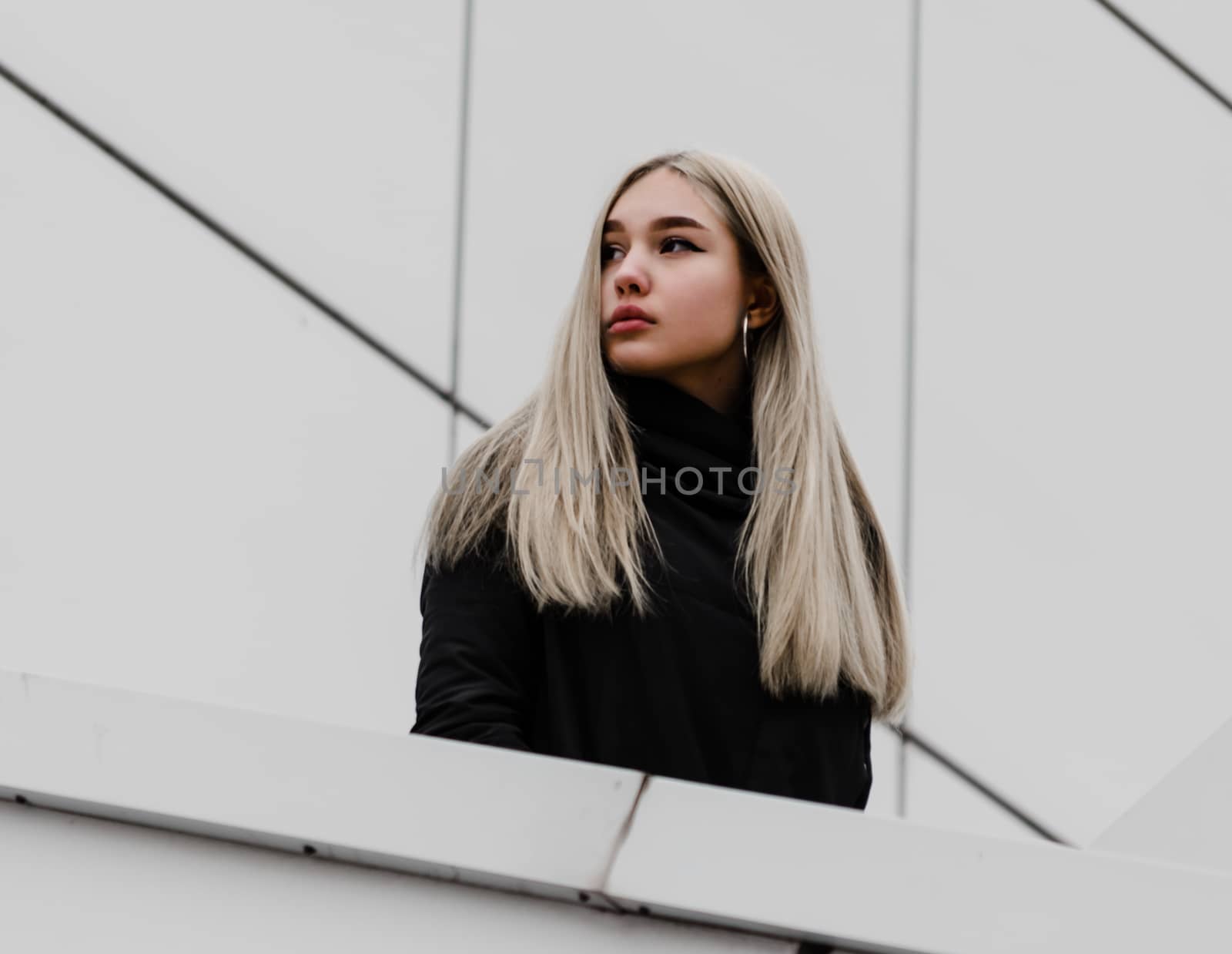 young blonde girl in black clothes against a gray building
