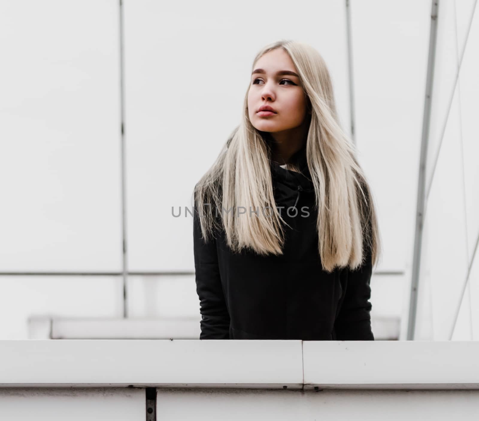 young blonde girl in black clothes against a gray building