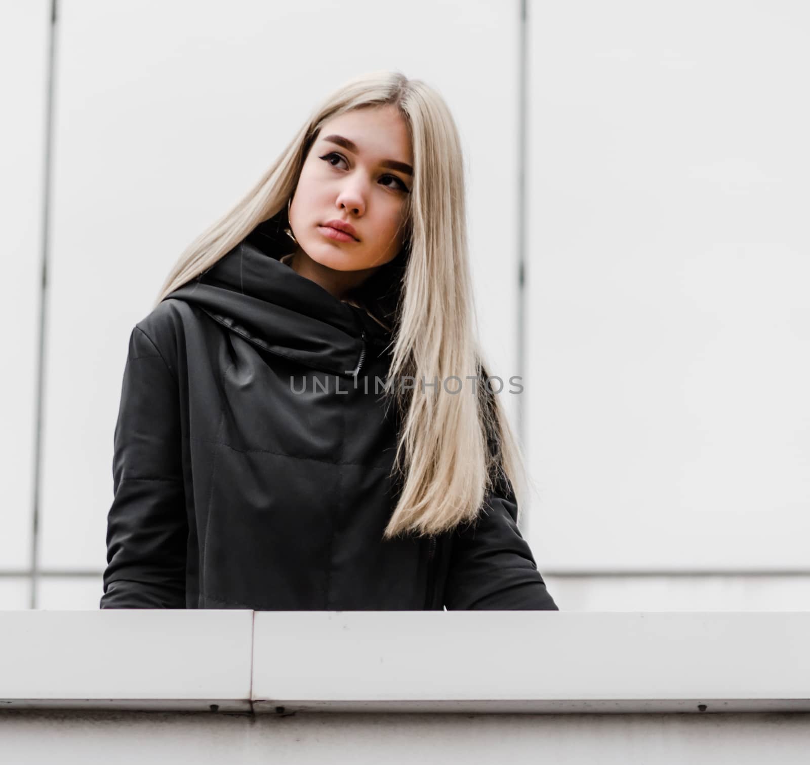 young blonde girl in black clothes against a gray building