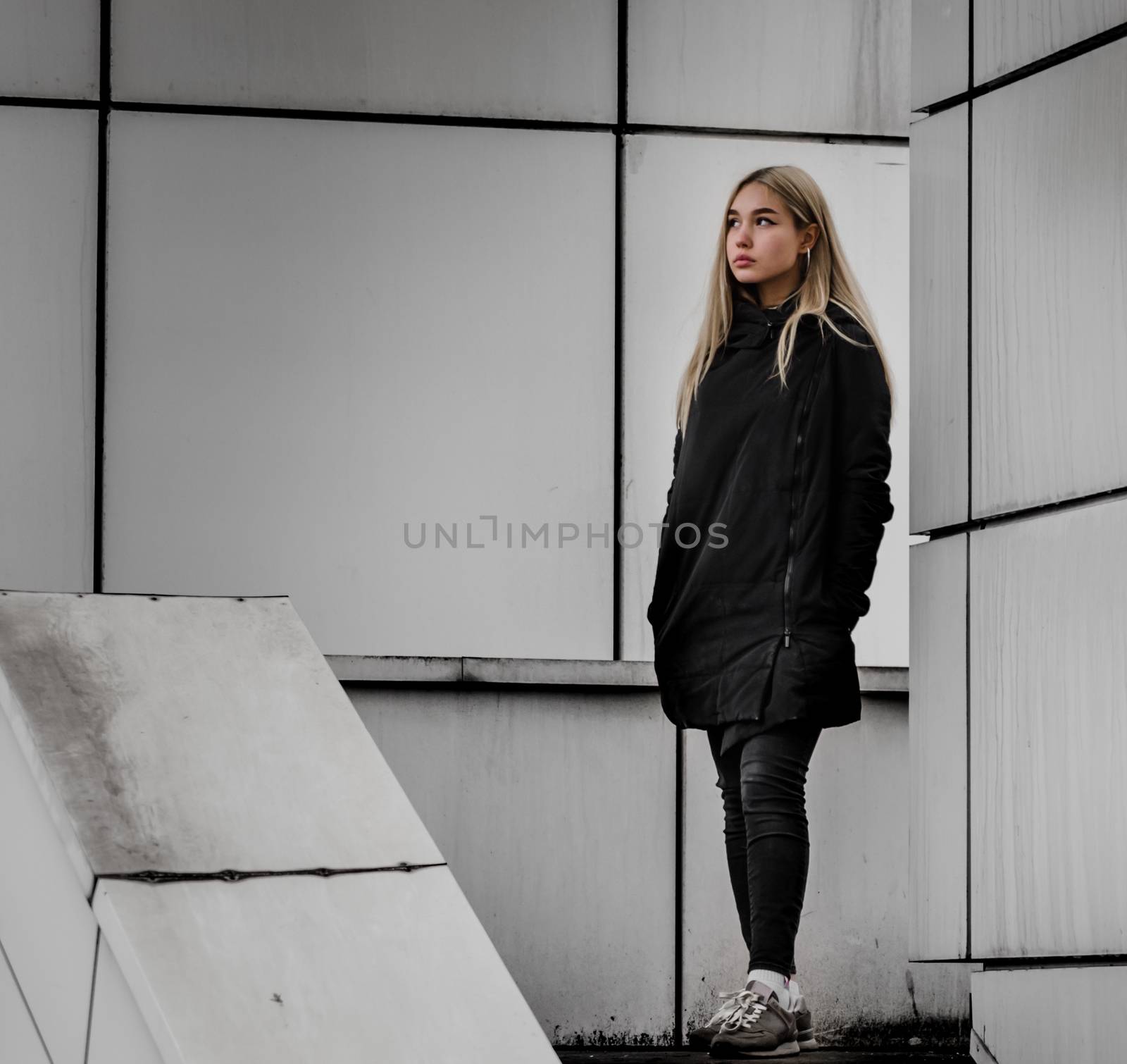 young blonde girl in black clothes against a gray building
