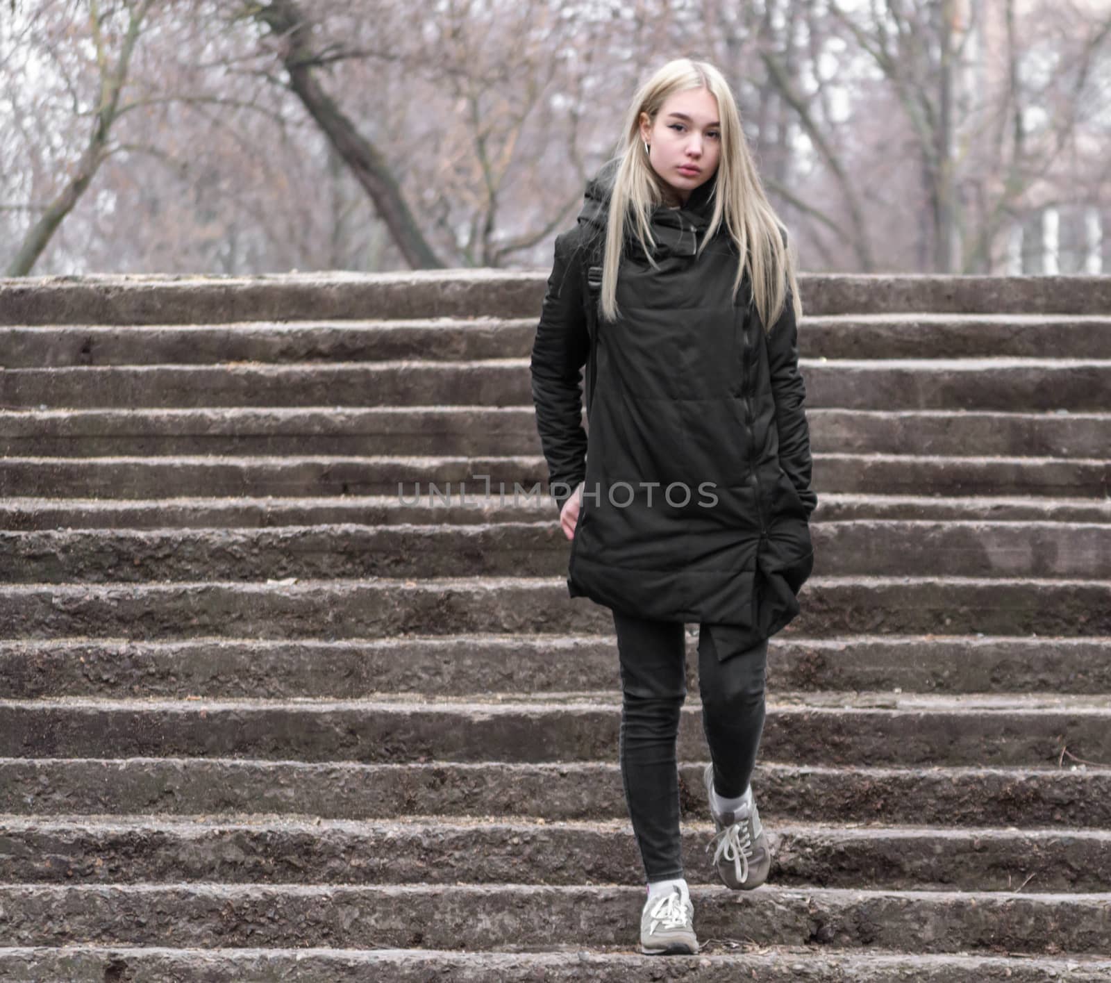 young blonde girl in black clothes comes down the stone stairs