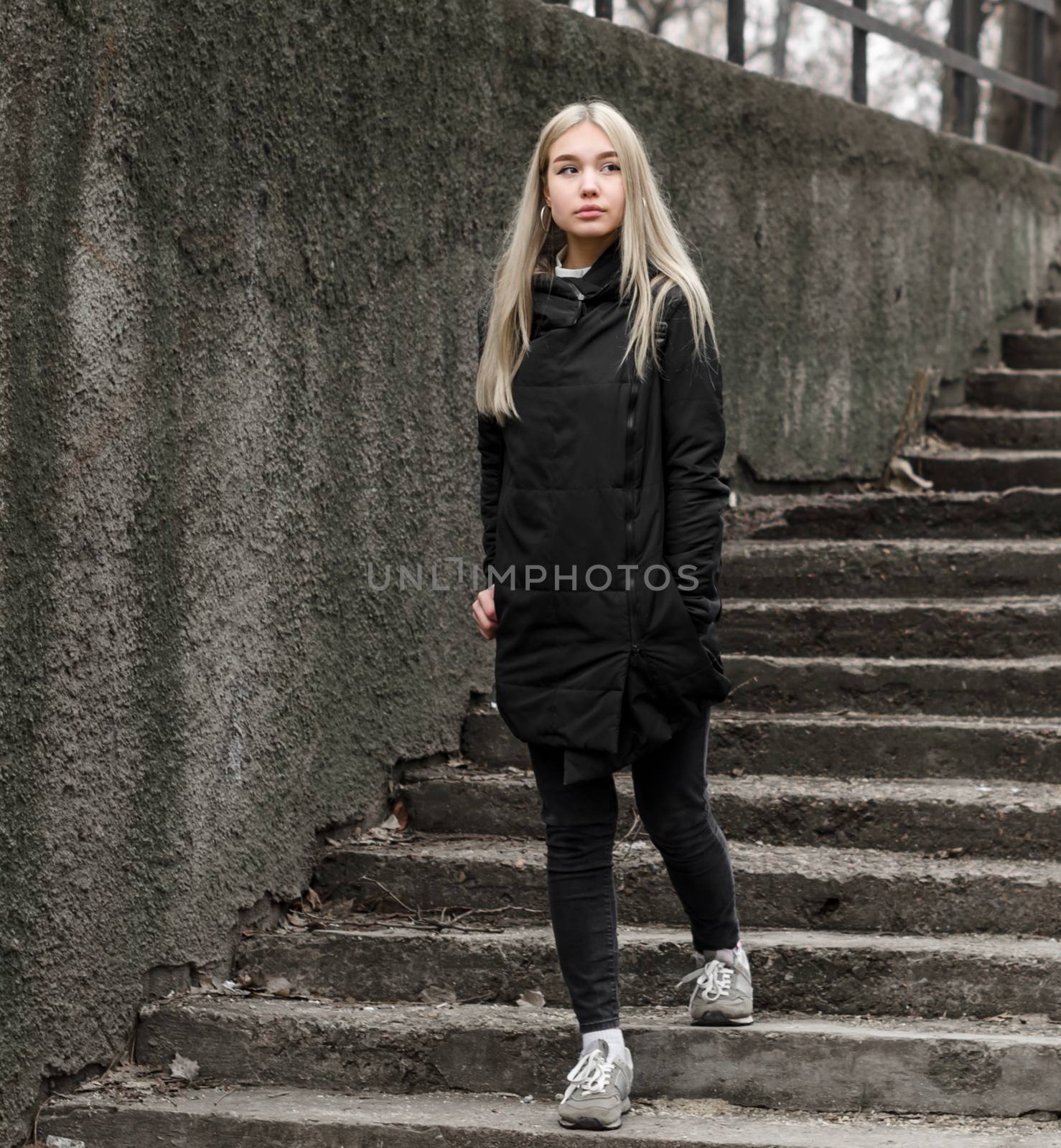 young blonde girl in black clothes comes down the stone stairs