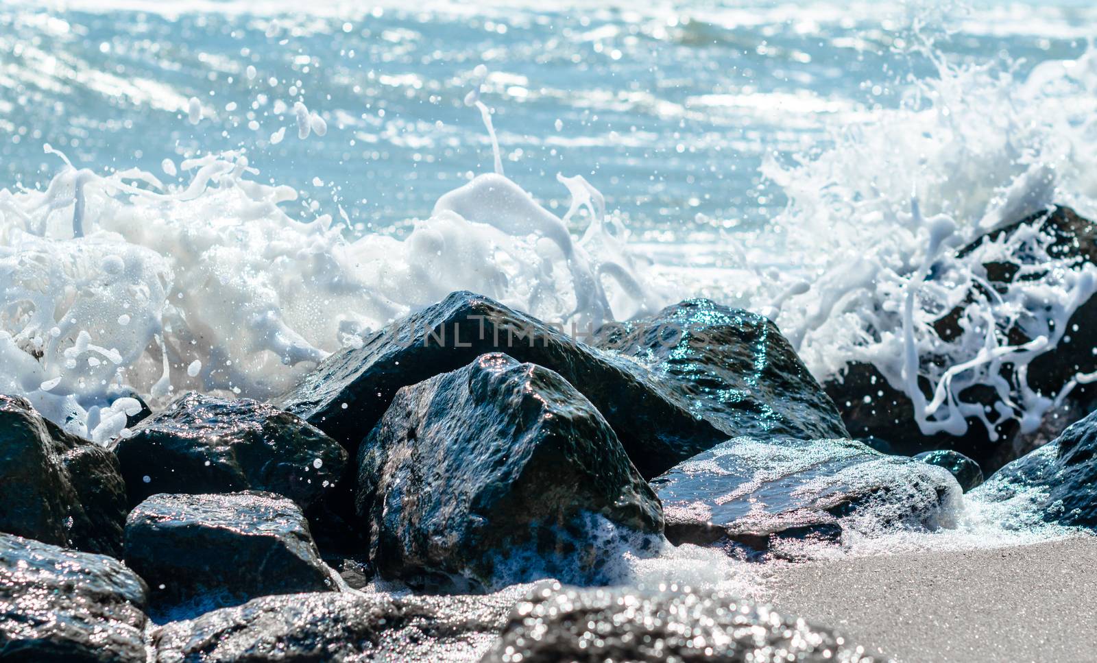 splashes of sea waves on the black stones on the sand of the beach