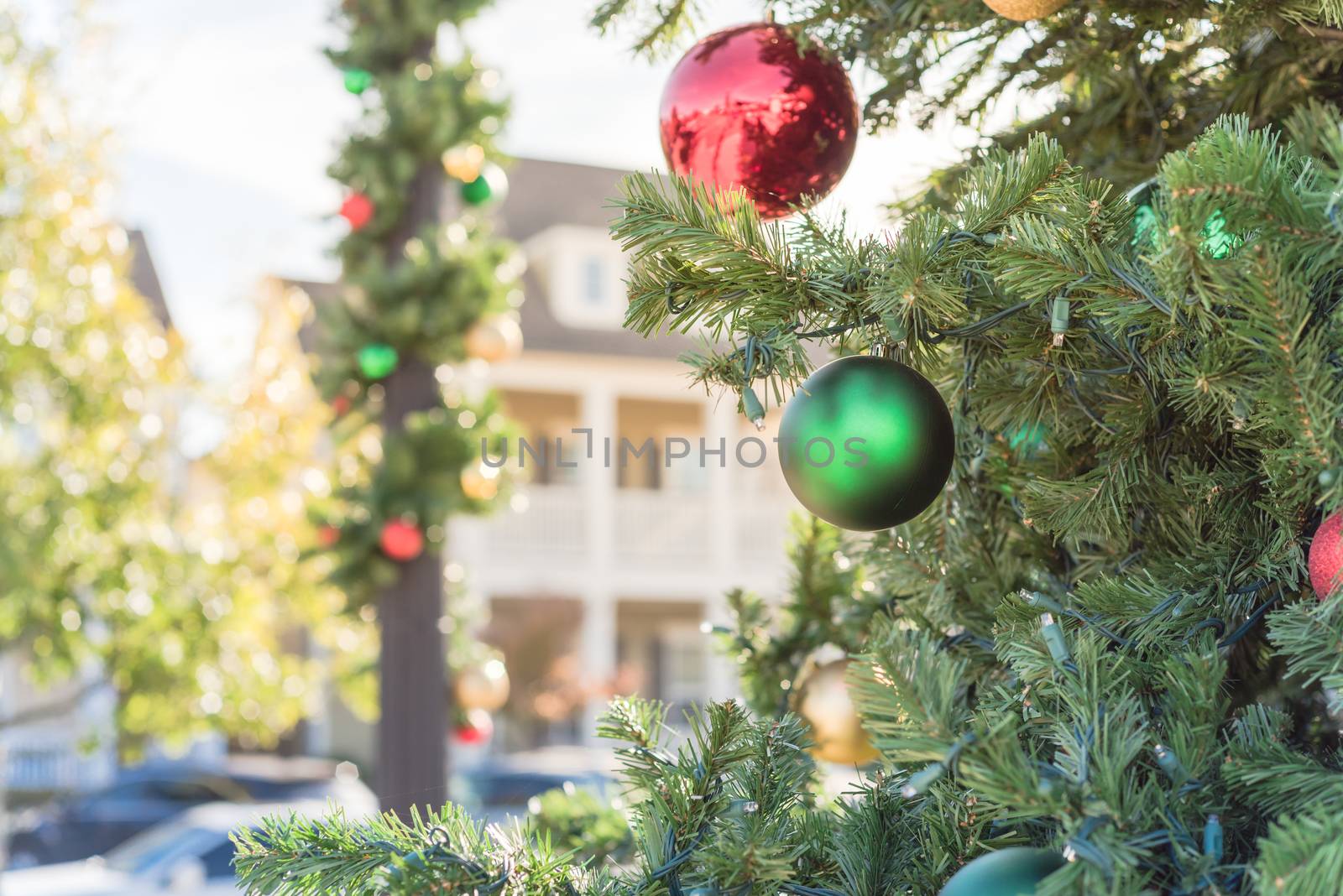 Beautiful Christmas ball hanging on pine branches at daytime light with two-story residential house in background. Baubles and spruce tree. Traditional artificial Xmas ornament near Dallas, Texas