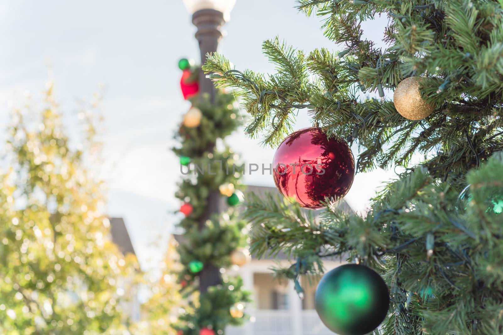 Beautiful Christmas ball hanging on pine branches at daytime light with two-story residential house in background. Baubles and spruce tree. Traditional artificial Xmas ornament near Dallas, Texas