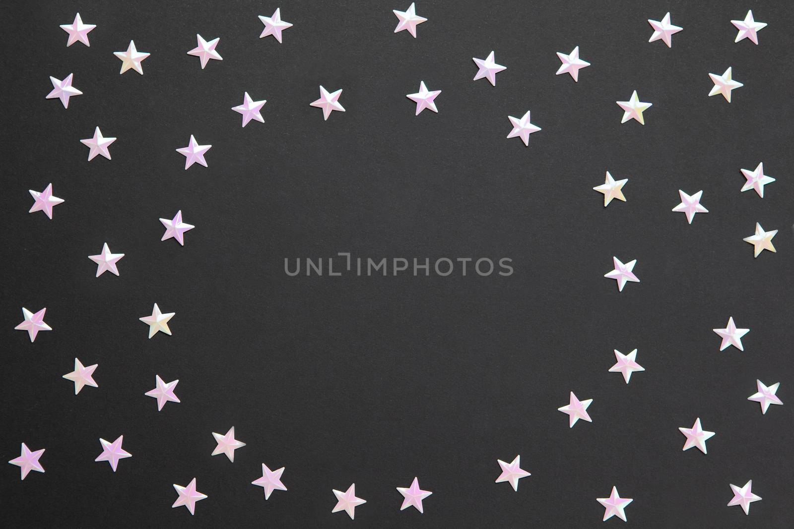 Frame of chaotic numerous pearl confetti in form of small stars on black paper background, copy space. Celebration, holidays, sales, fashion concept. Horizontal. Flatlay. Blank for greeting cards.