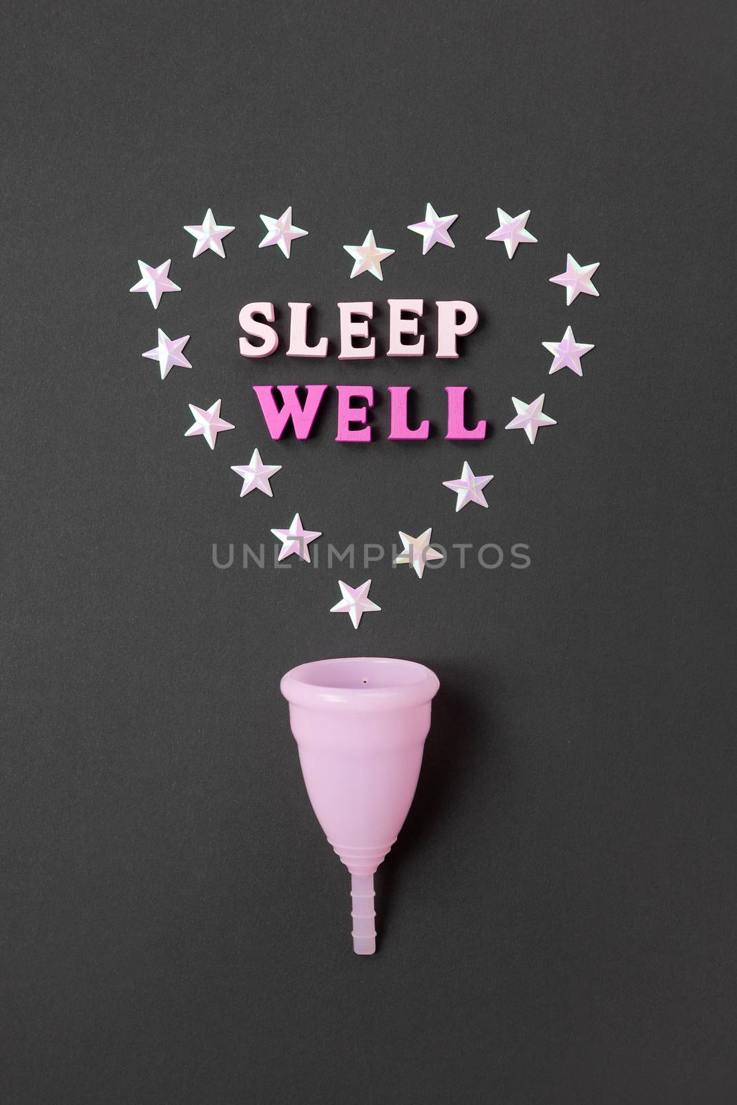 Pink menstrual cup on black background with with heart and words Sleep Well. Concept possibility of use cup at night, zero waste, savings, minimalism. Feminine hygiene product, flat lay. Vertical.