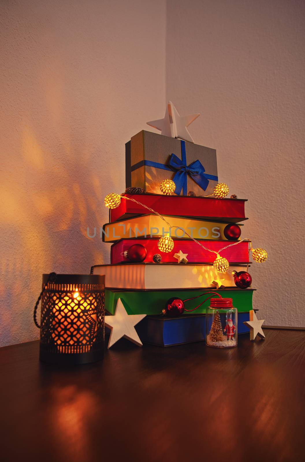 Christmas tree made of stacked colourful books decorated with ornaments, lights and cute gift placed on a table at home or bookstore or library. Christmas and New Year composition with books.