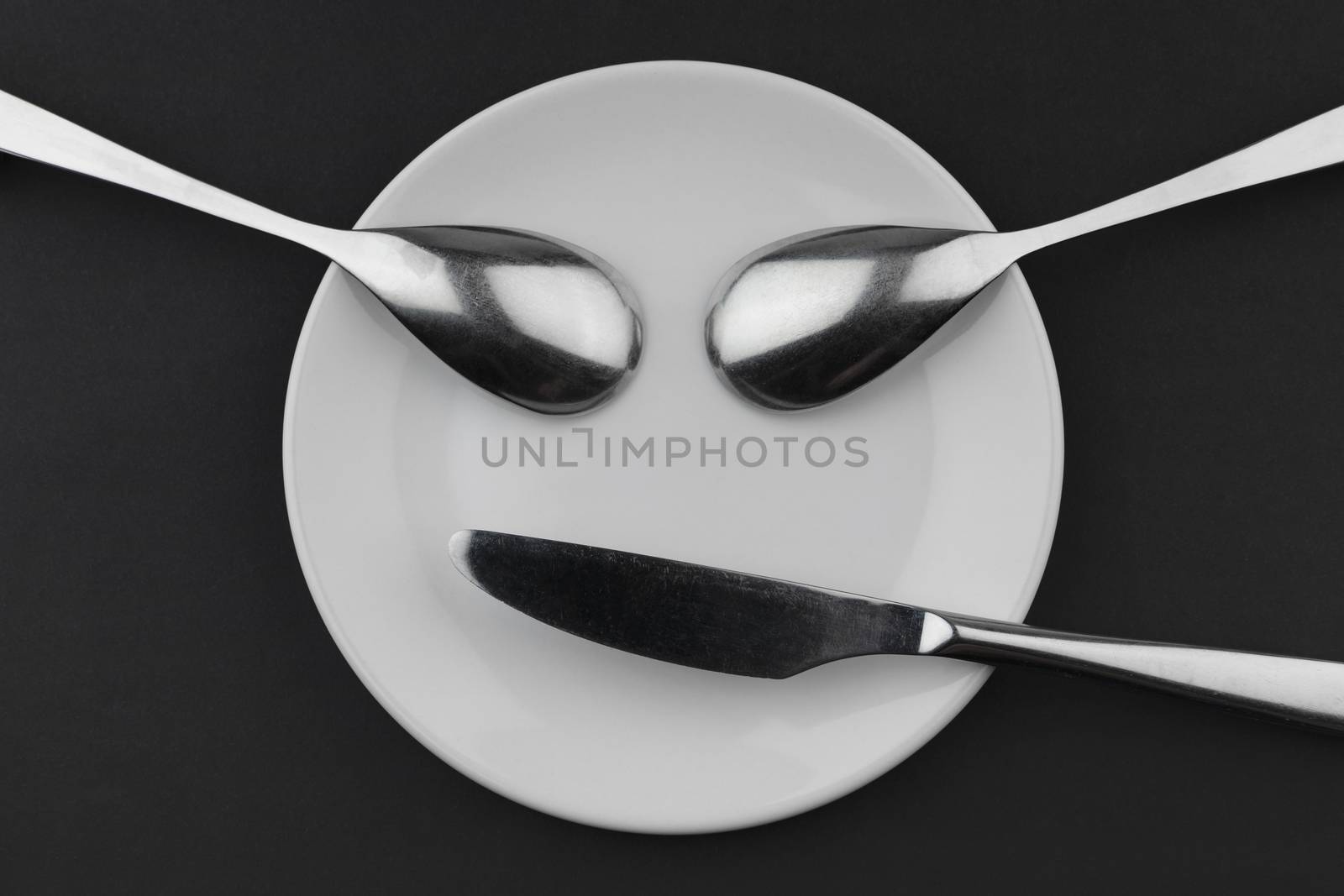 Conceptual face of a ceramic board two metal spoons and a knife
