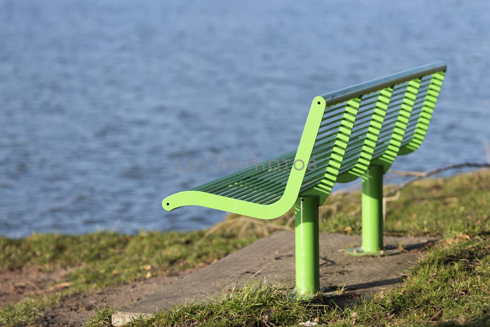 Green bench as street furniture in a grassy area on the waterfront
