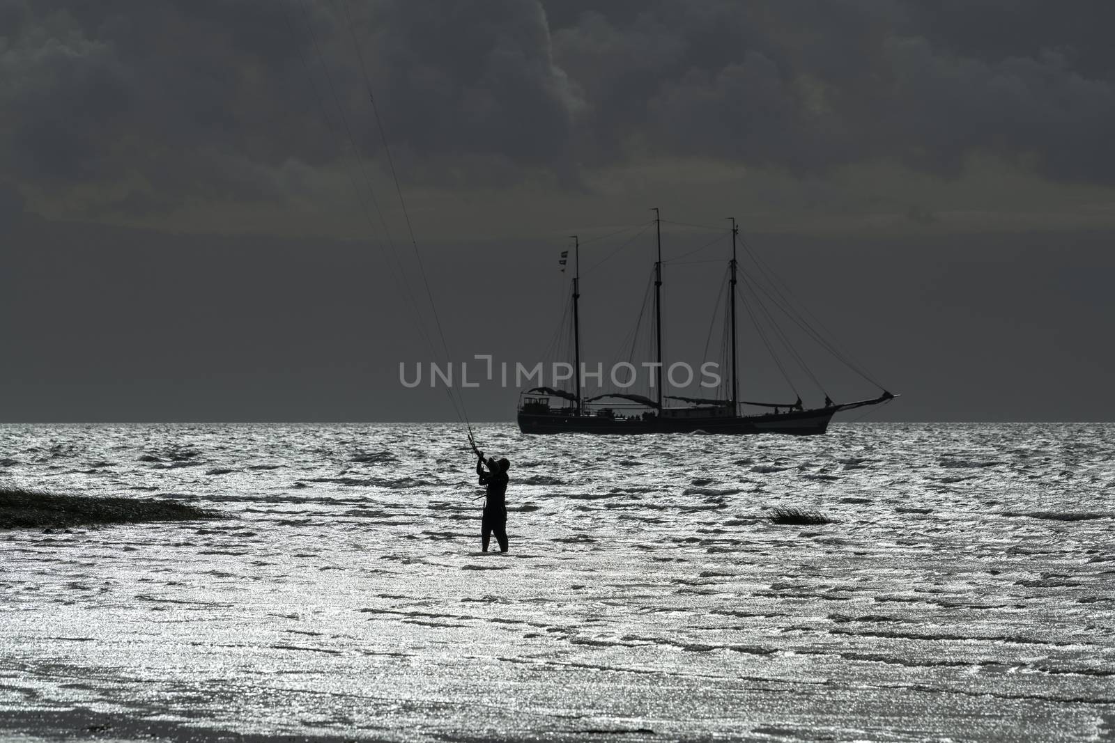 Contour of a three-masted sailboat and a kite surfer on the Wadden Sea near the island of Terschelling in the North of the Netherlands
