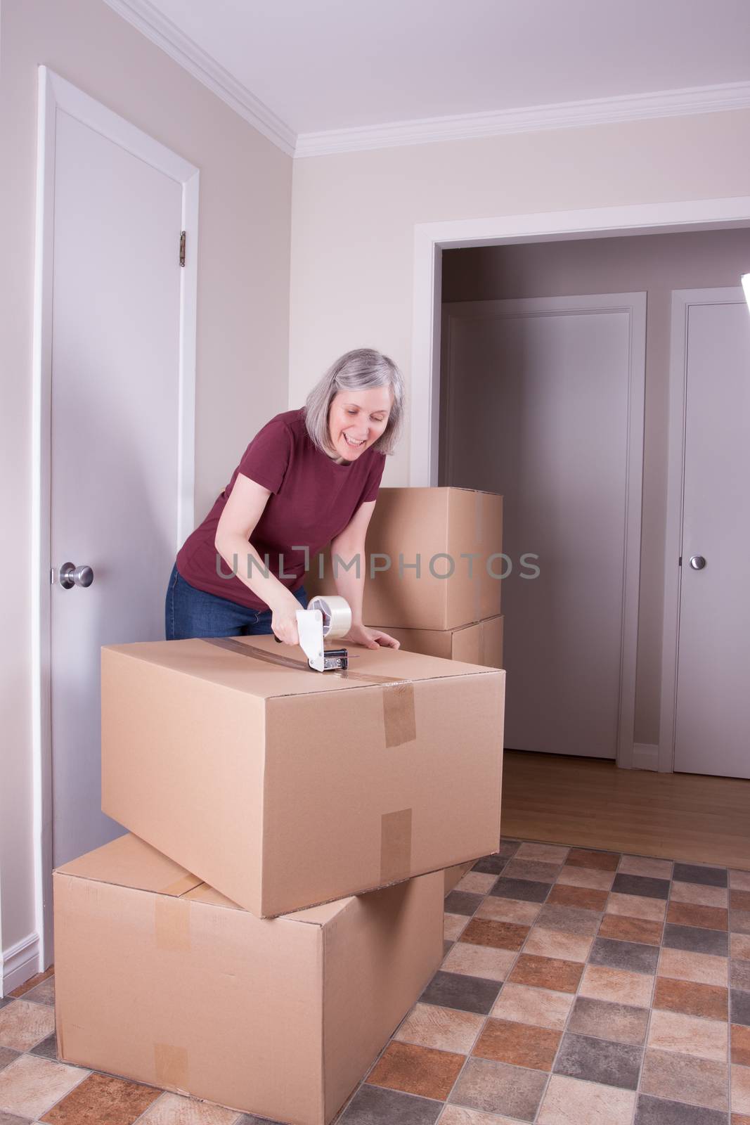 Woman in her early fifties closing a cardboard box with tape for moving it to other house