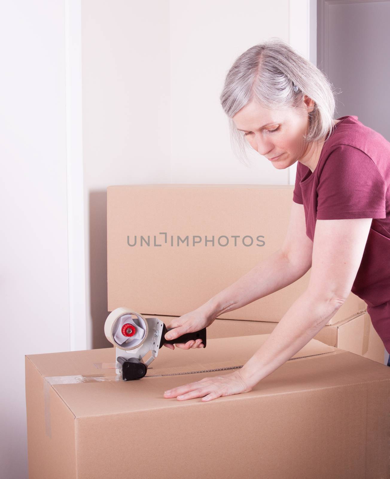 Woman in her fifties closing a big box with tape, ready to move to other house