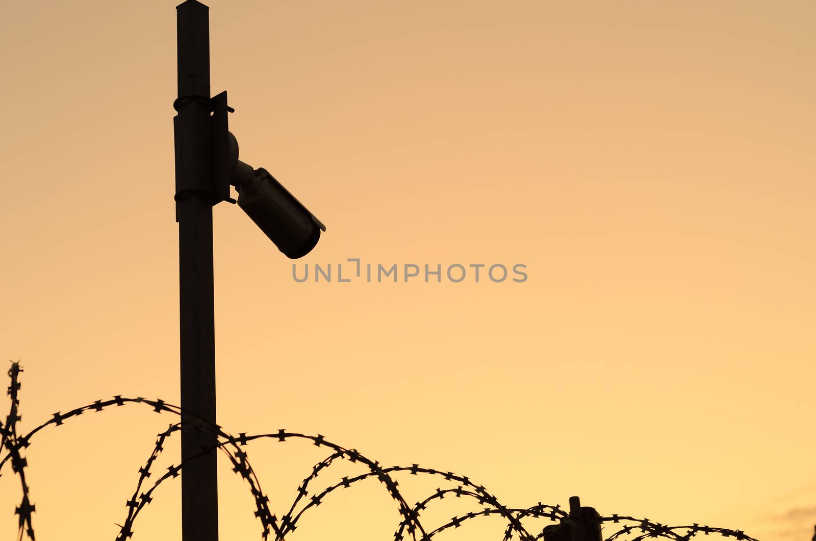 Silhouette of the Security camera on the pole on sunset.Observation of the perimeter of the protected area with barbed wire.Space for text