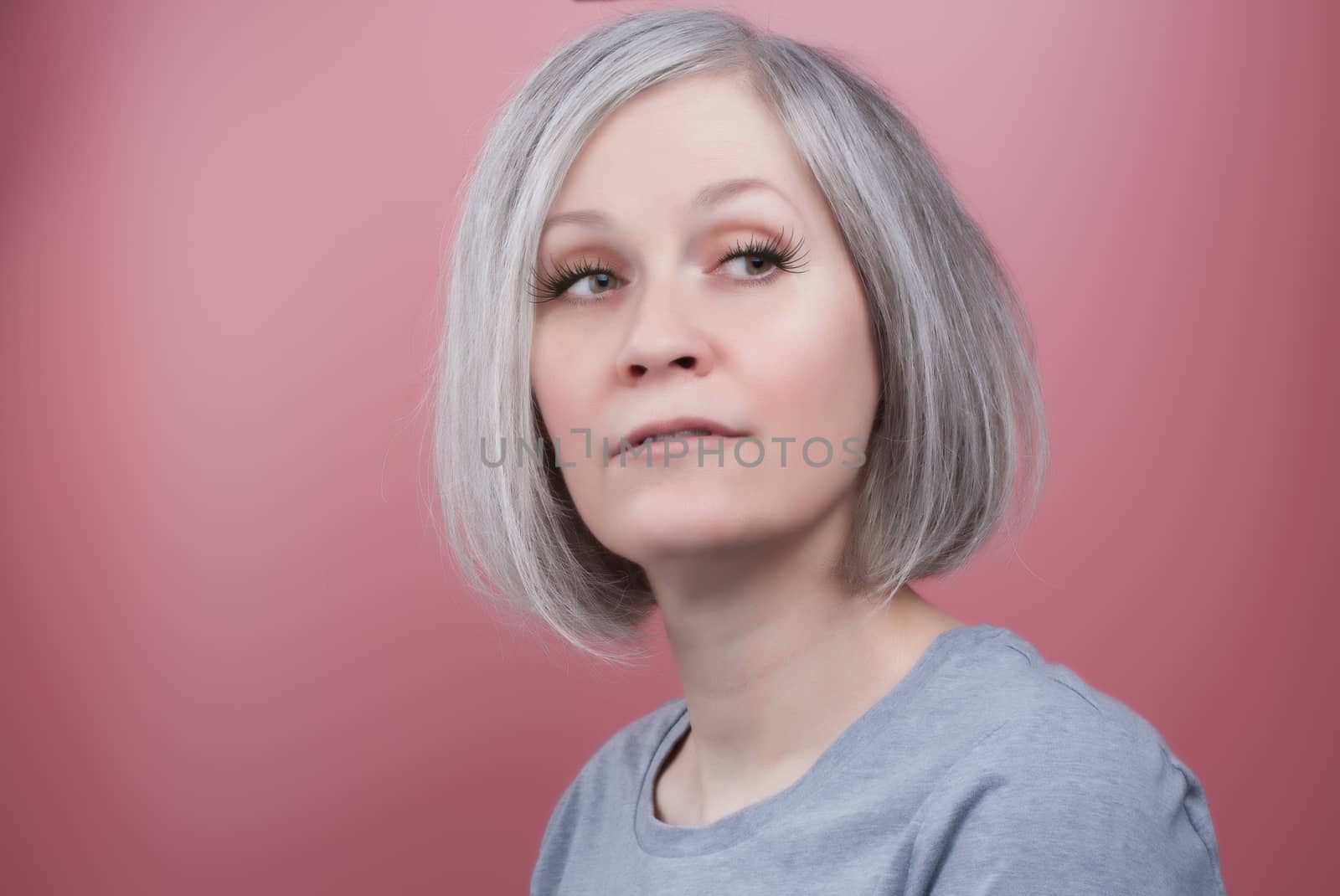 Beautiful woman in her early fifties wearing fake lashes, pink background