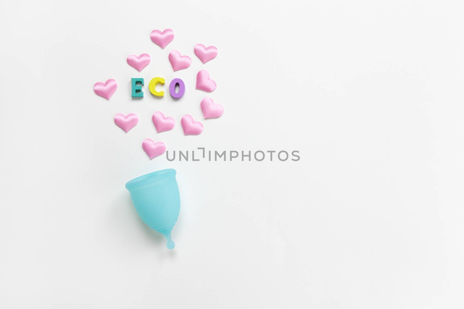 Turquoise menstrual cup on white background with hearts and word Eco from colorful wooden letters. Concept zero waste, savings, minimalism. Feminine hygiene product flat lay, copy space. Horizontal.