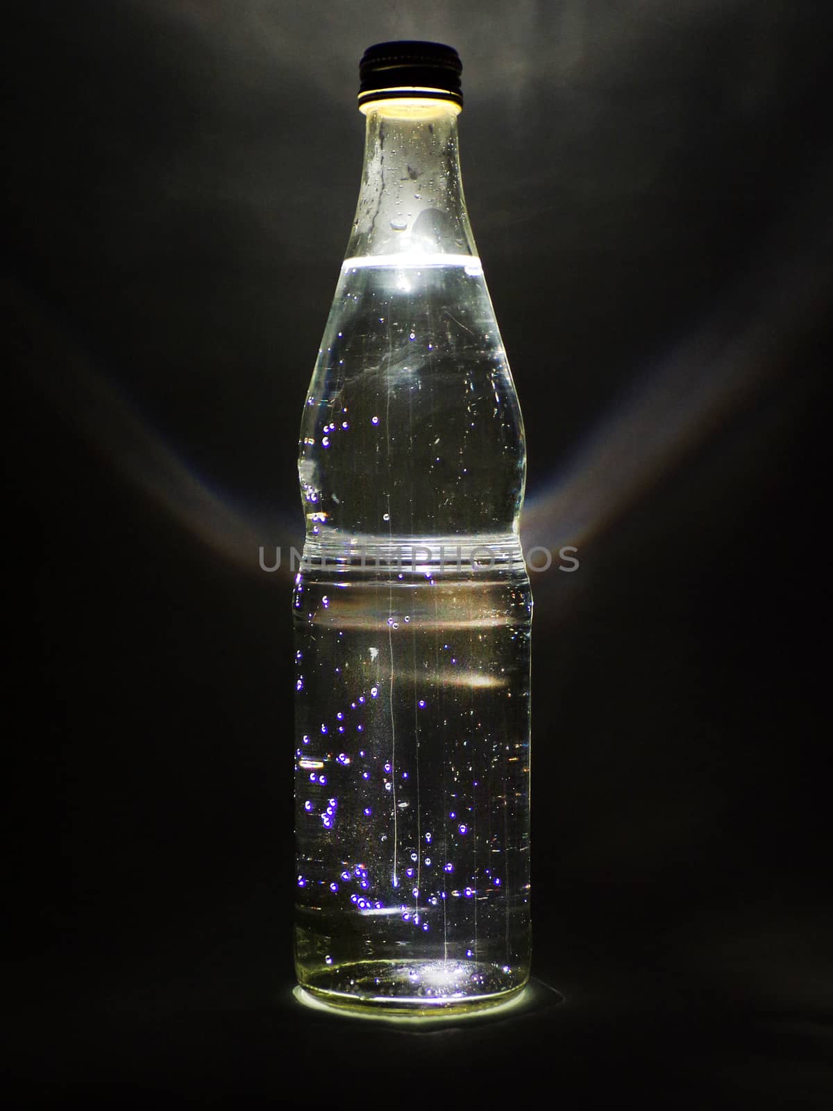 Glass bottle with drink and backlight on black background.