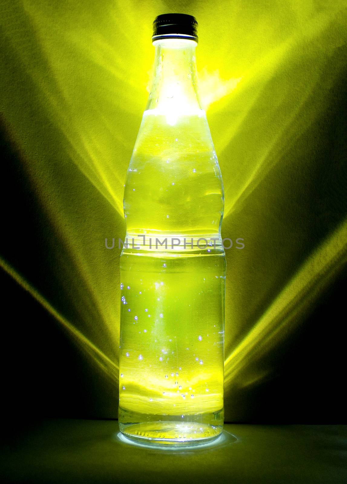 Bottle of mineral water behind yellow background. Healthy diet and healthy lifestyle. Cold water in a glass bottle with water drops on it.