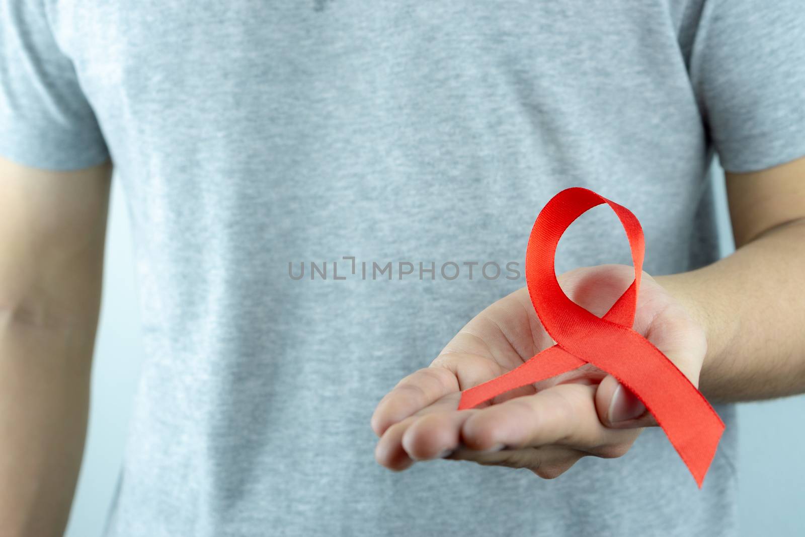 Aids awareness, male hands holding red AIDS awareness ribbon. World Aids Day, Healthcare and medical concept.