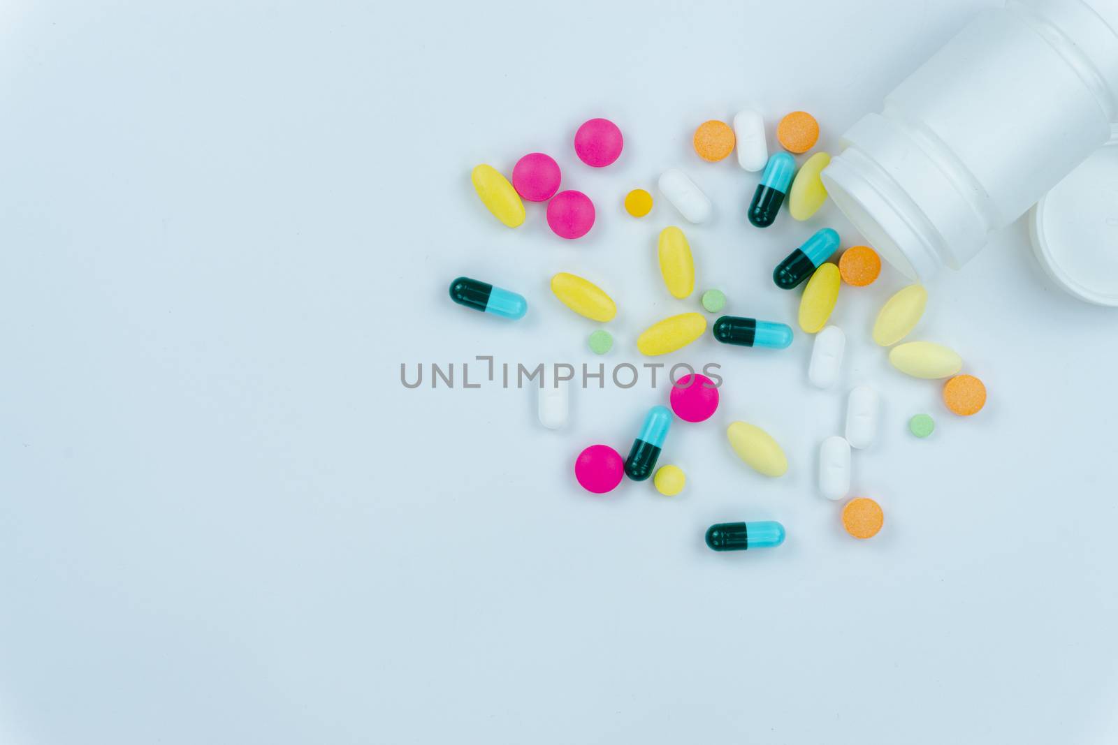 Assorted pharmaceutical medicine pills, tablets and capsules, and bottle on white background. Copy space for text, top view.