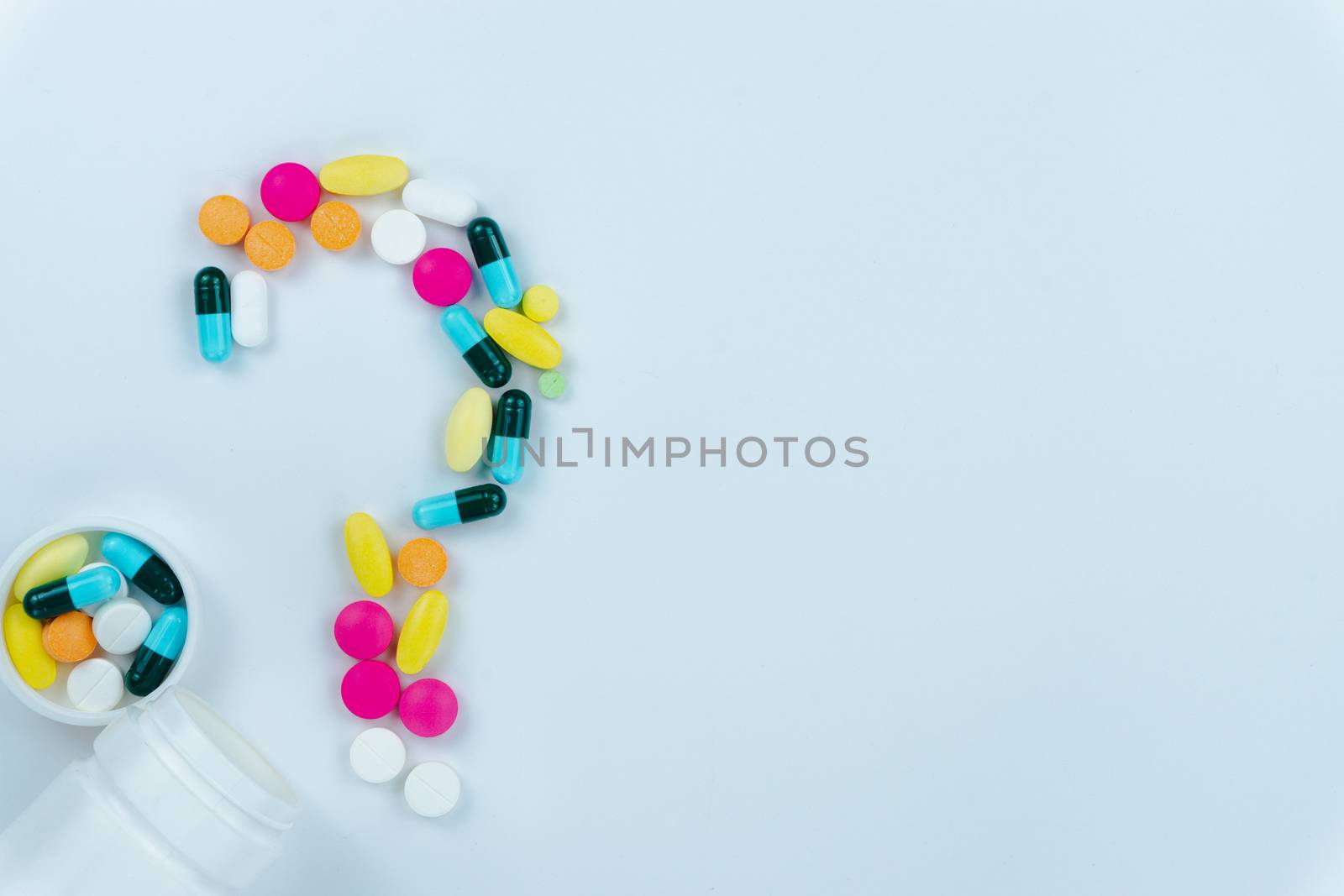 Assorted pharmaceutical medicine pills with question sign, tablets and capsules, and bottle on white background. Copy space for text, top view.