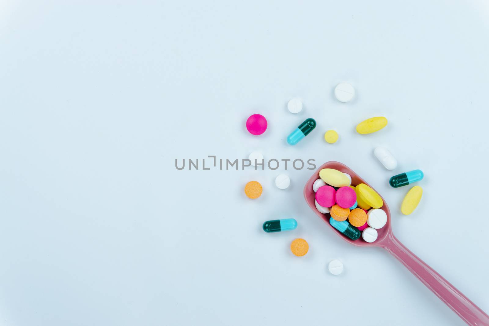 Assorted pharmaceutical medicine pills, tablets and capsules, and spoon on white background. Copy space for text, top view.