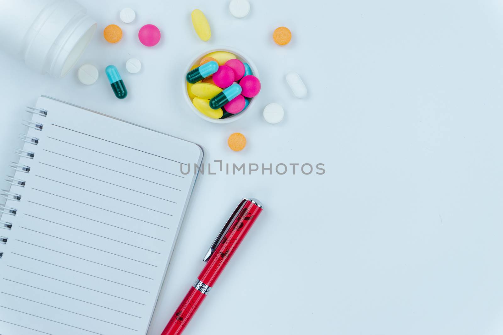 Assorted pharmaceutical medicine pills, tablets and capsules, pen and paper note on white background. Copy space for text, top view.