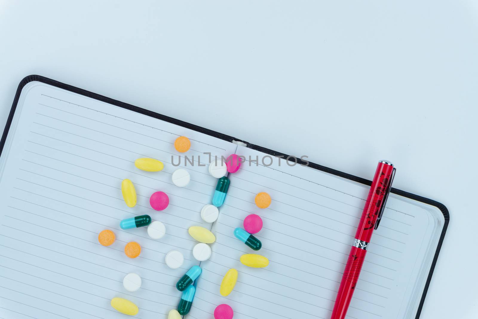 Assorted pharmaceutical medicine pills, tablets and capsules, pen and paper note on white background. Copy space for text, top view.